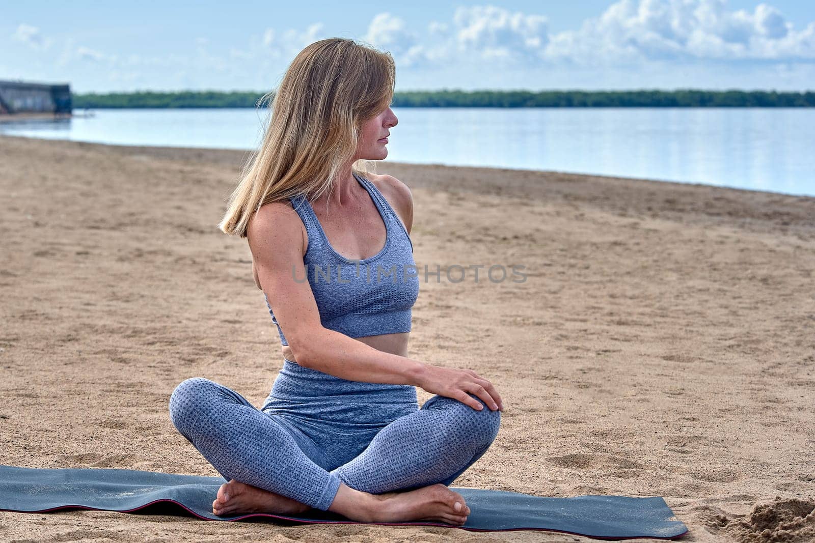 A woman does yoga on a sandy beach against the background of a river. High quality photo