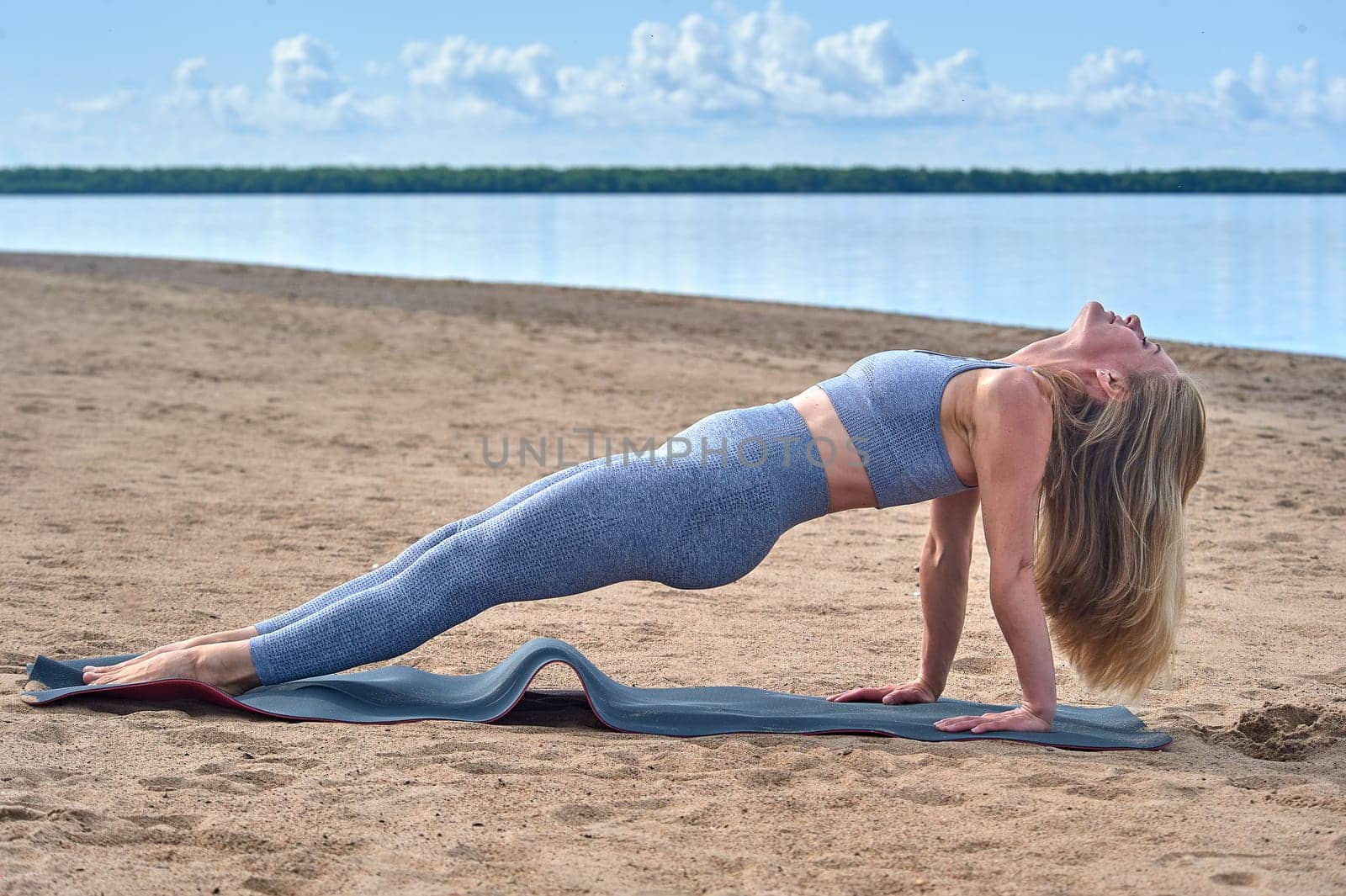 A woman does yoga on a sandy beach against the background of a river. High quality photo