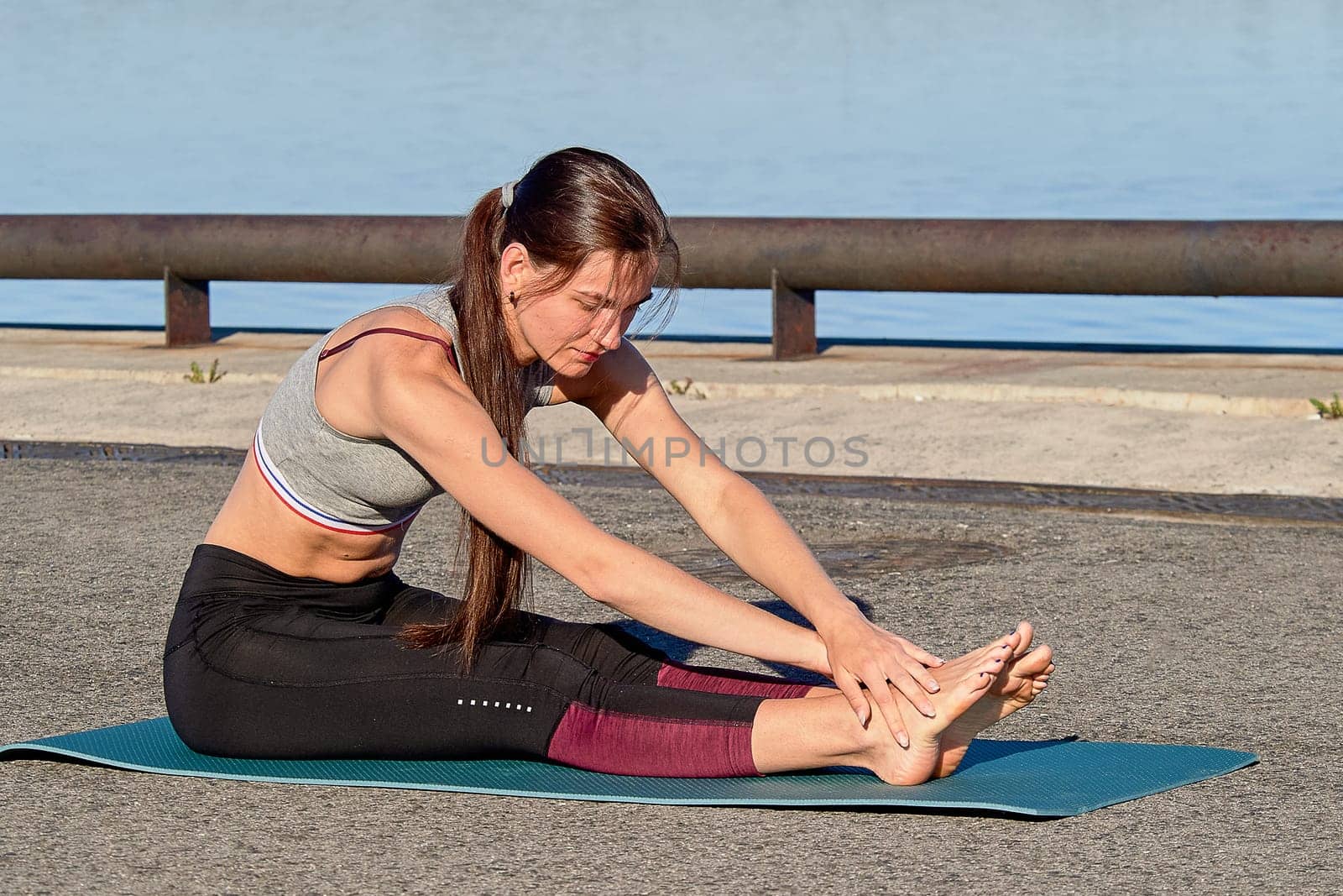 A young woman does a warm-up on the pier in the early morning, against the background of the river. High quality photo