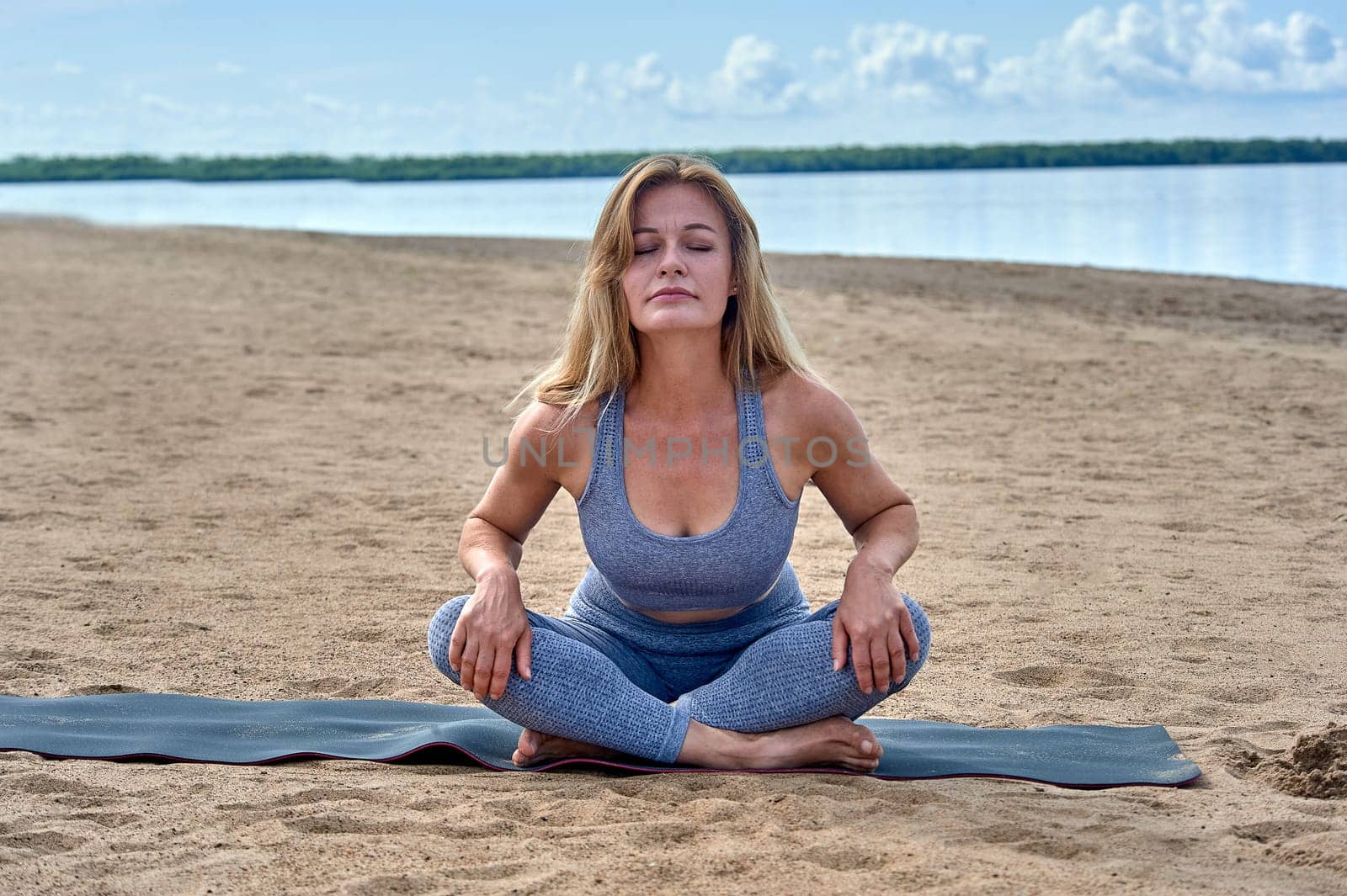A woman does yoga on a sandy beach against the background of a river. High quality photo