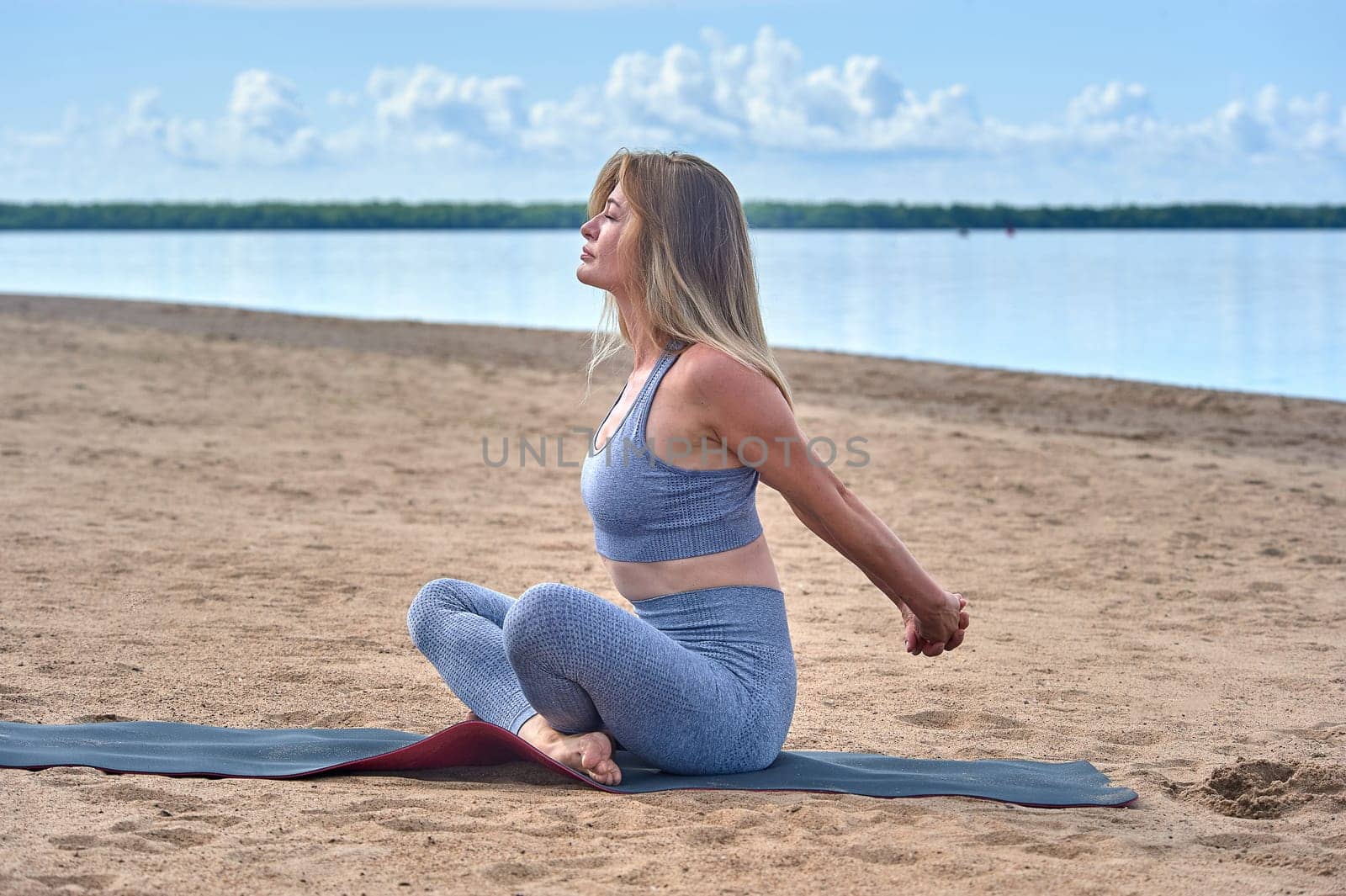 A woman does yoga on a sandy beach against the background of a river. High quality photo