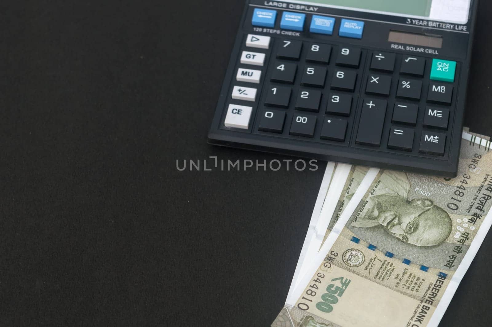 Indian Rupee placed under a calculator on table. Isolated on black background.