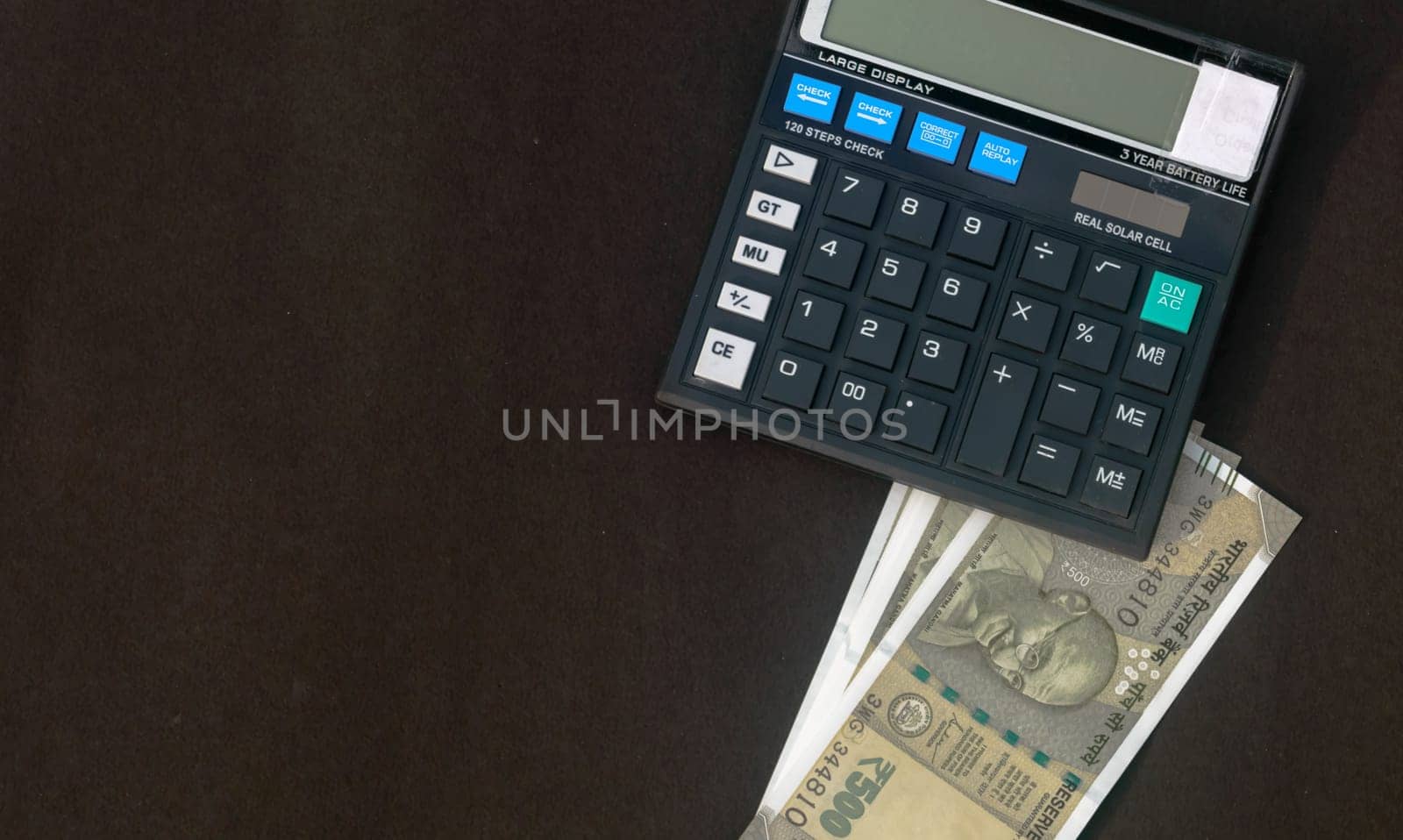 Indian Rupee placed under a calculator on table. Isolated on grey background.