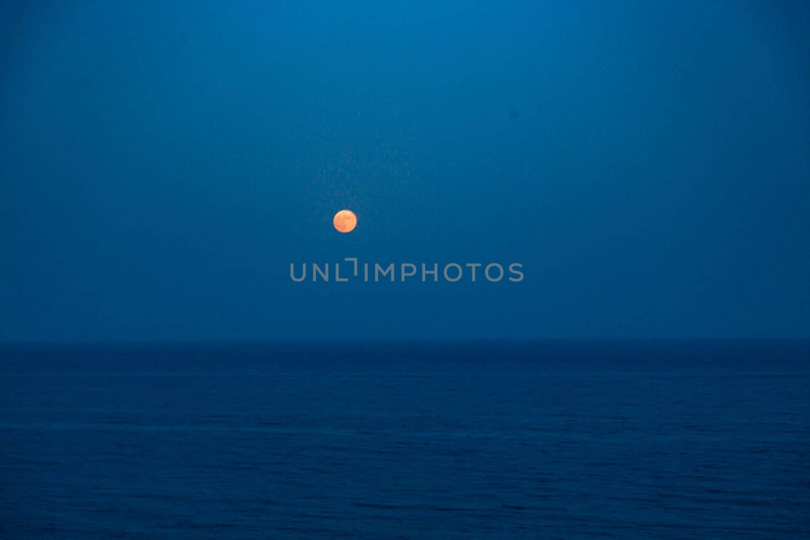 Full Red Moon Glows Brightly in the Blue Sky on a Evening Over the Sea.