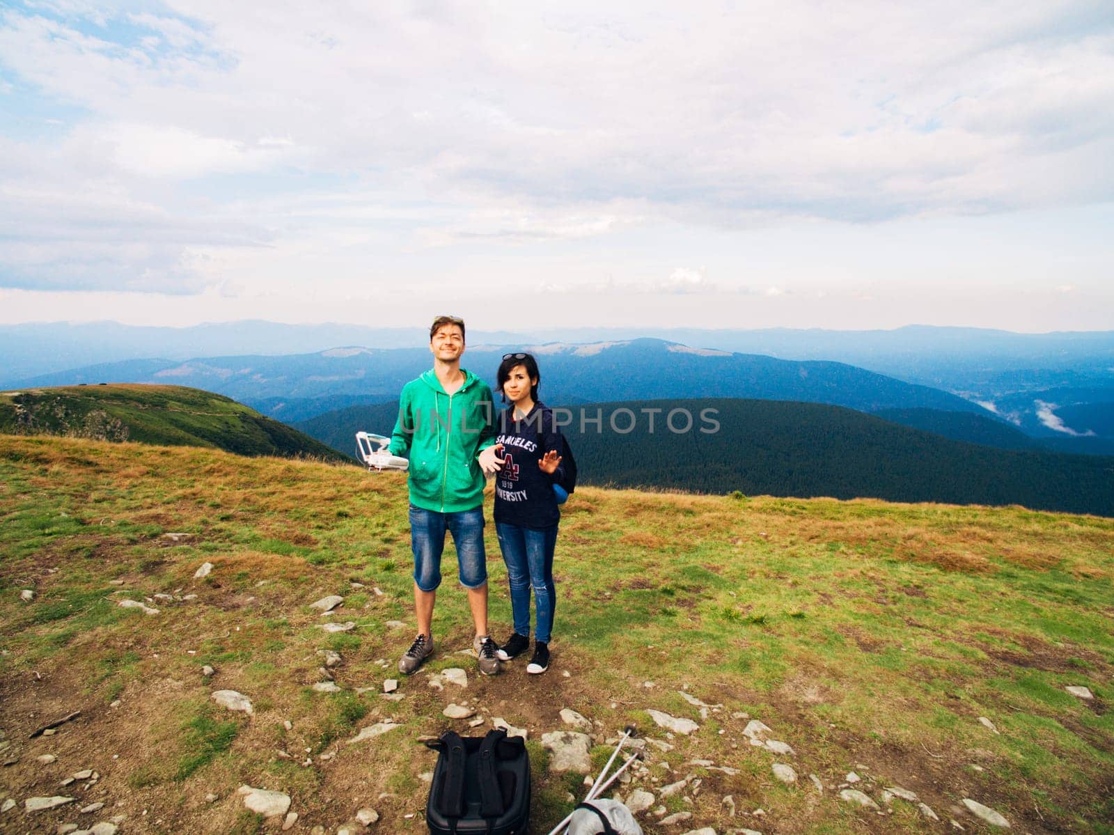 Aerial view of the Great Green Ridge. Guy and Girl Standing on a Big Hill against the Backdrop of a Huge Mountain Landscape.