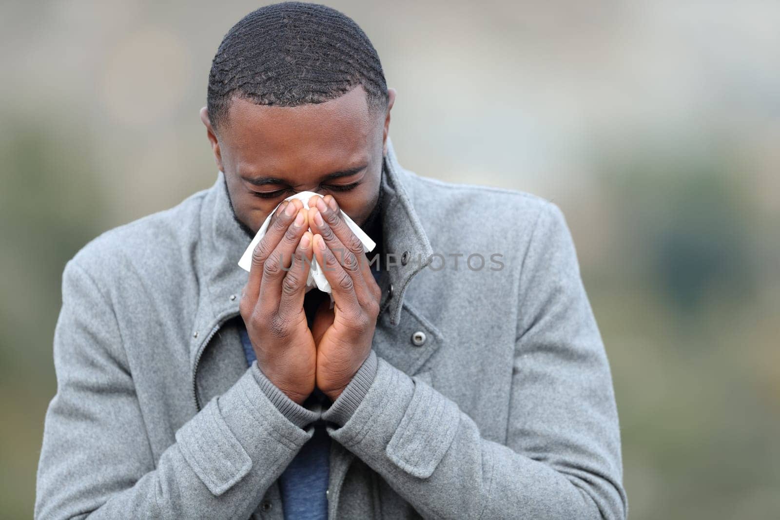 Ill man with black skin blowing on tissue