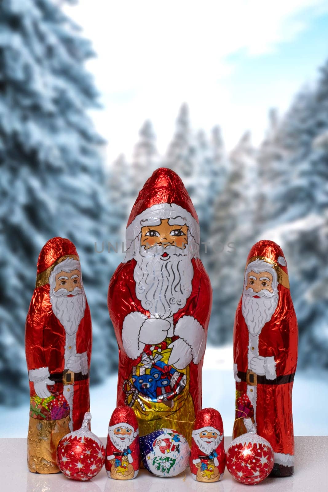Christmas greeting card. Closeup of various cheerful wrapped chocolate Santa Claus over festive abstract blurred winter landscape. Xmas and New Year gift sweets. Macro.