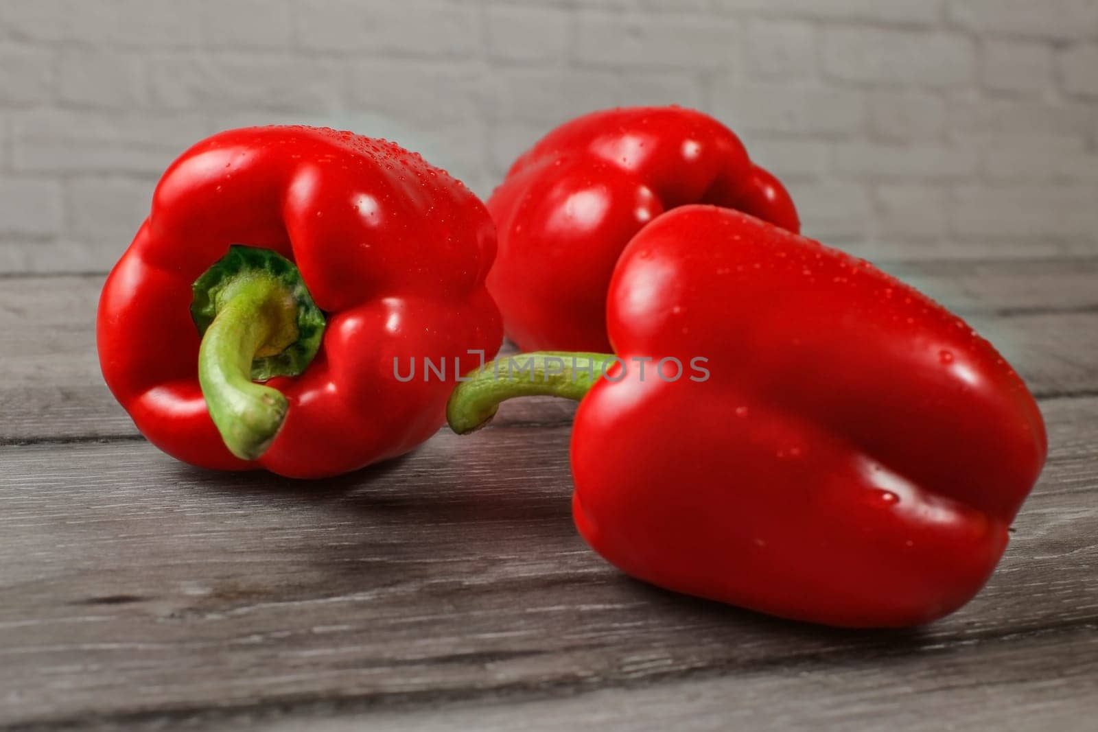 Three bright red bell peppers on wooden desk, focus to water drops.