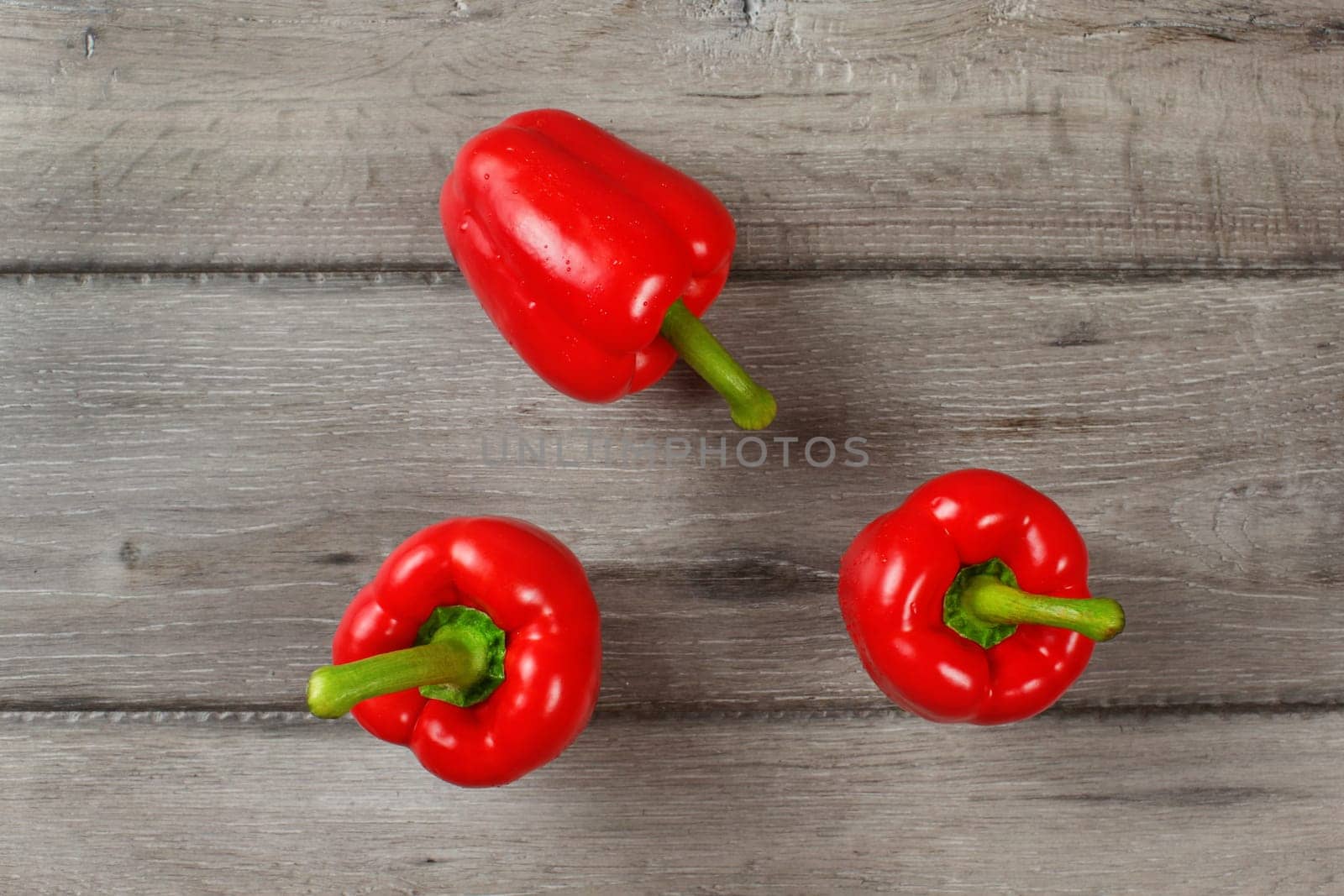 Tabletop view - three red bell peppers on gray wood desk.