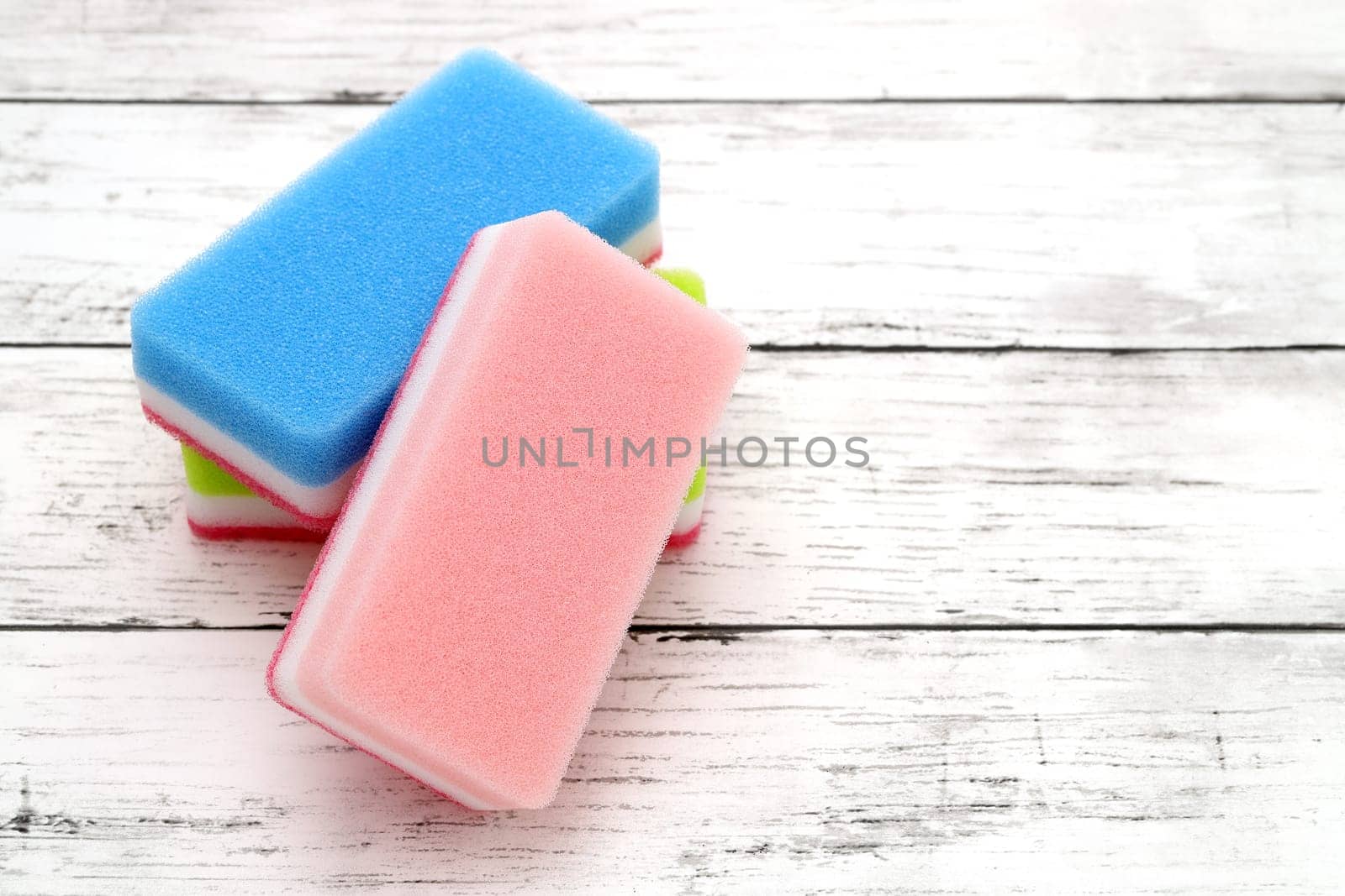 color rectangular sponges for washing dishes and cleaning on white wooden background