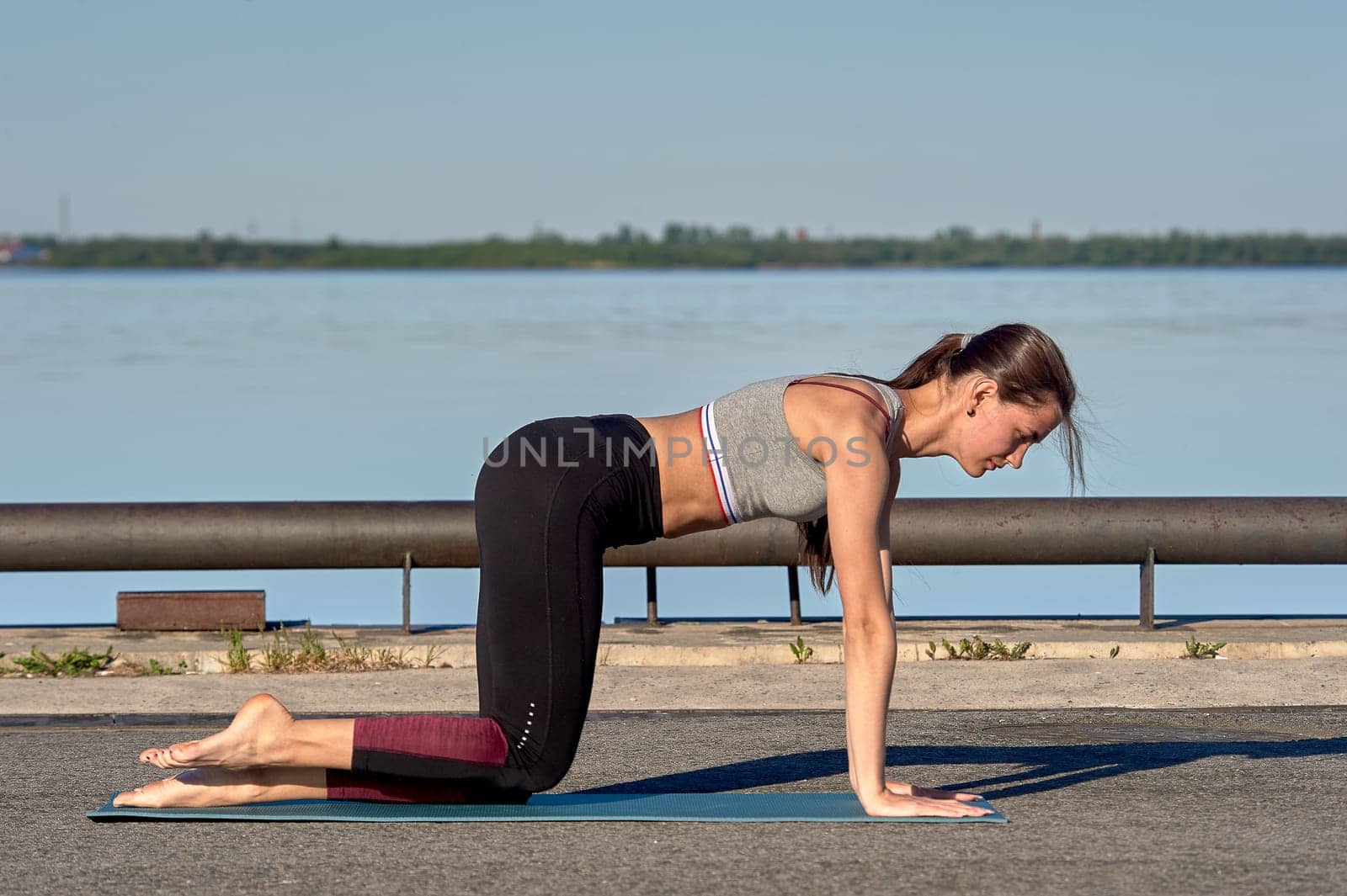 A young woman does a warm-up on the pier in the early morning, against the background of the river. High quality photo