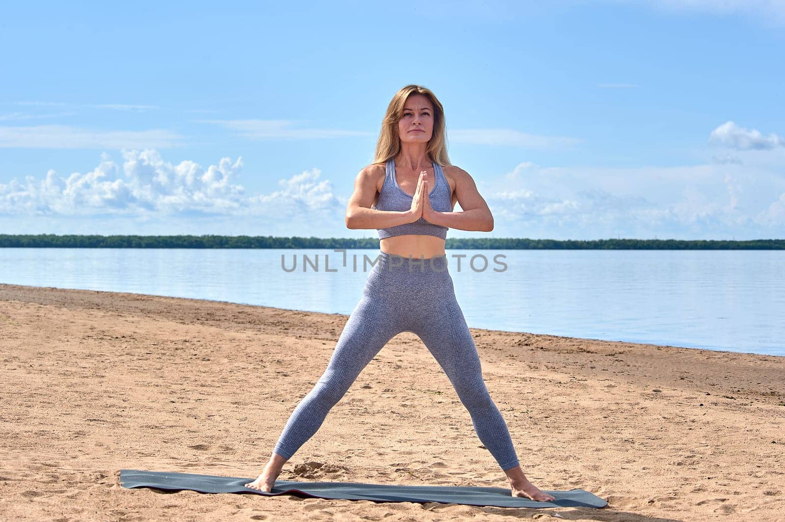 A woman does yoga on a sandy beach against the background of a river. High quality photo