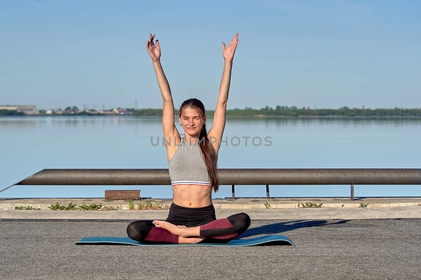 A young woman does a warm-up on the pier in the early morning, against the background of the river. High quality photo