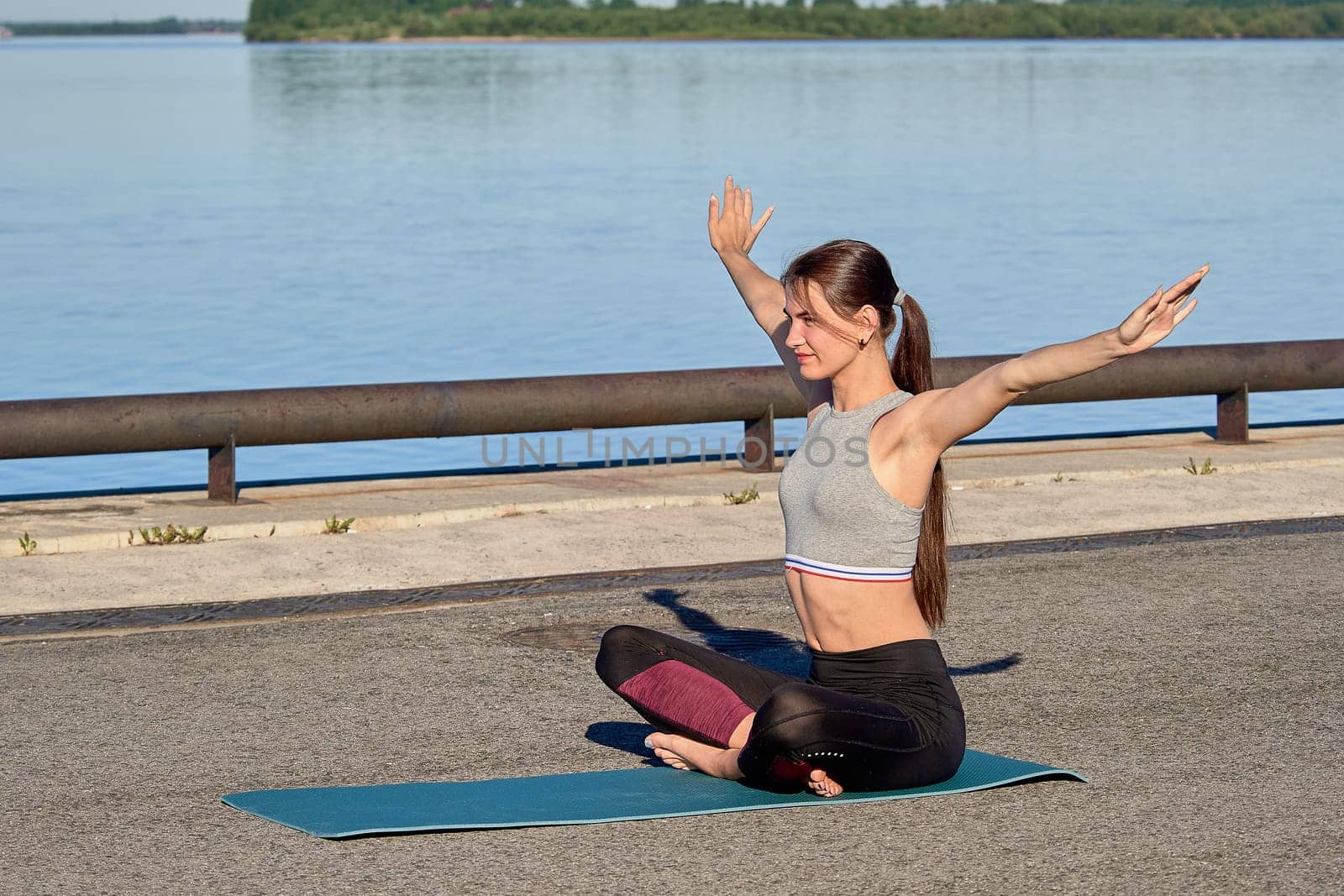 A young woman does a warm-up on the pier in the early morning, against the background of the river. High quality photo