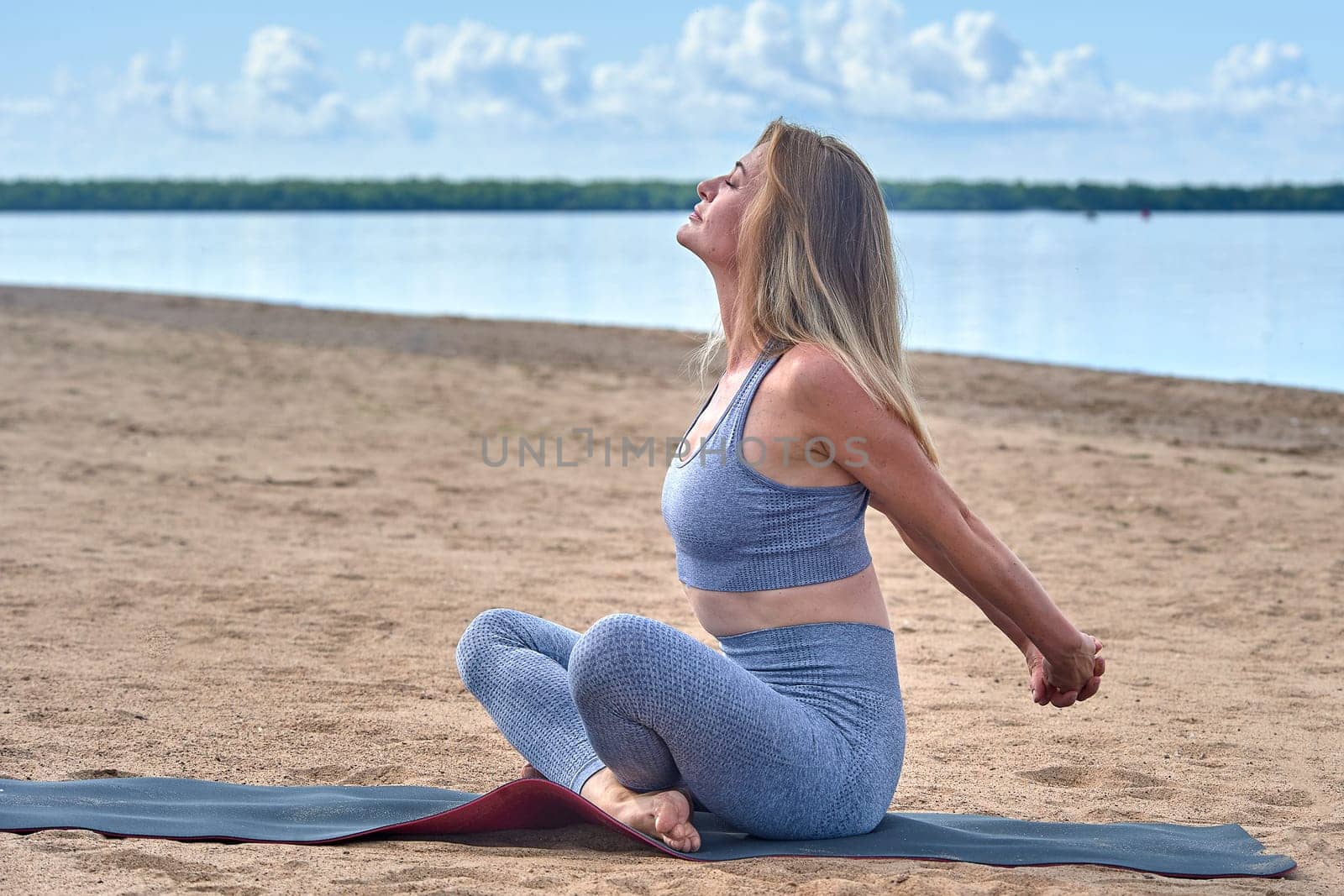 A woman does yoga on a sandy beach against the background of a river. High quality photo