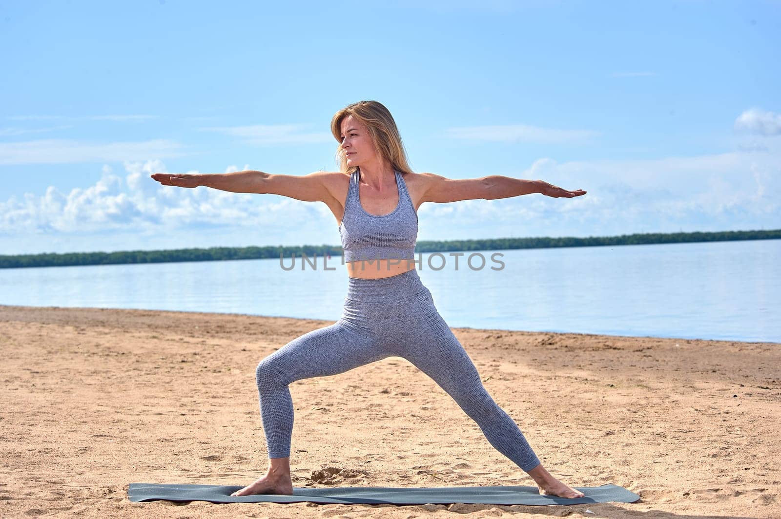 A woman does yoga on a sandy beach against the background of a river. High quality photo