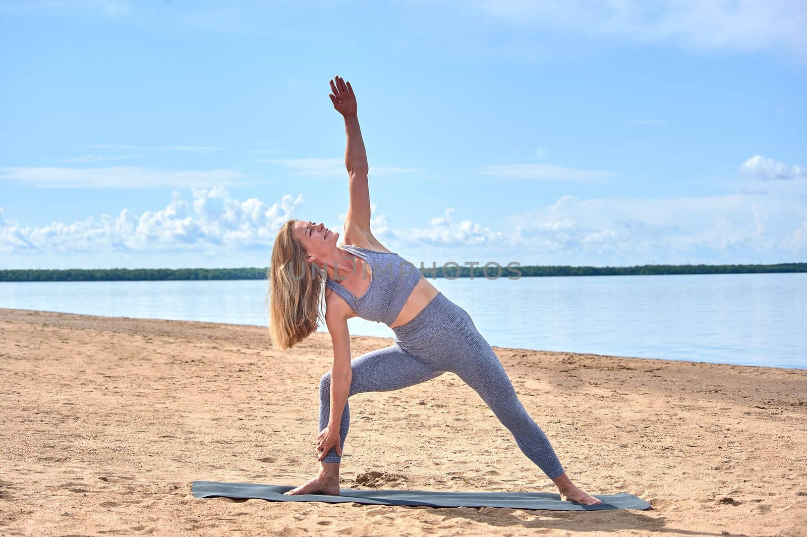 A woman does yoga on a sandy beach against the background of a river. High quality photo