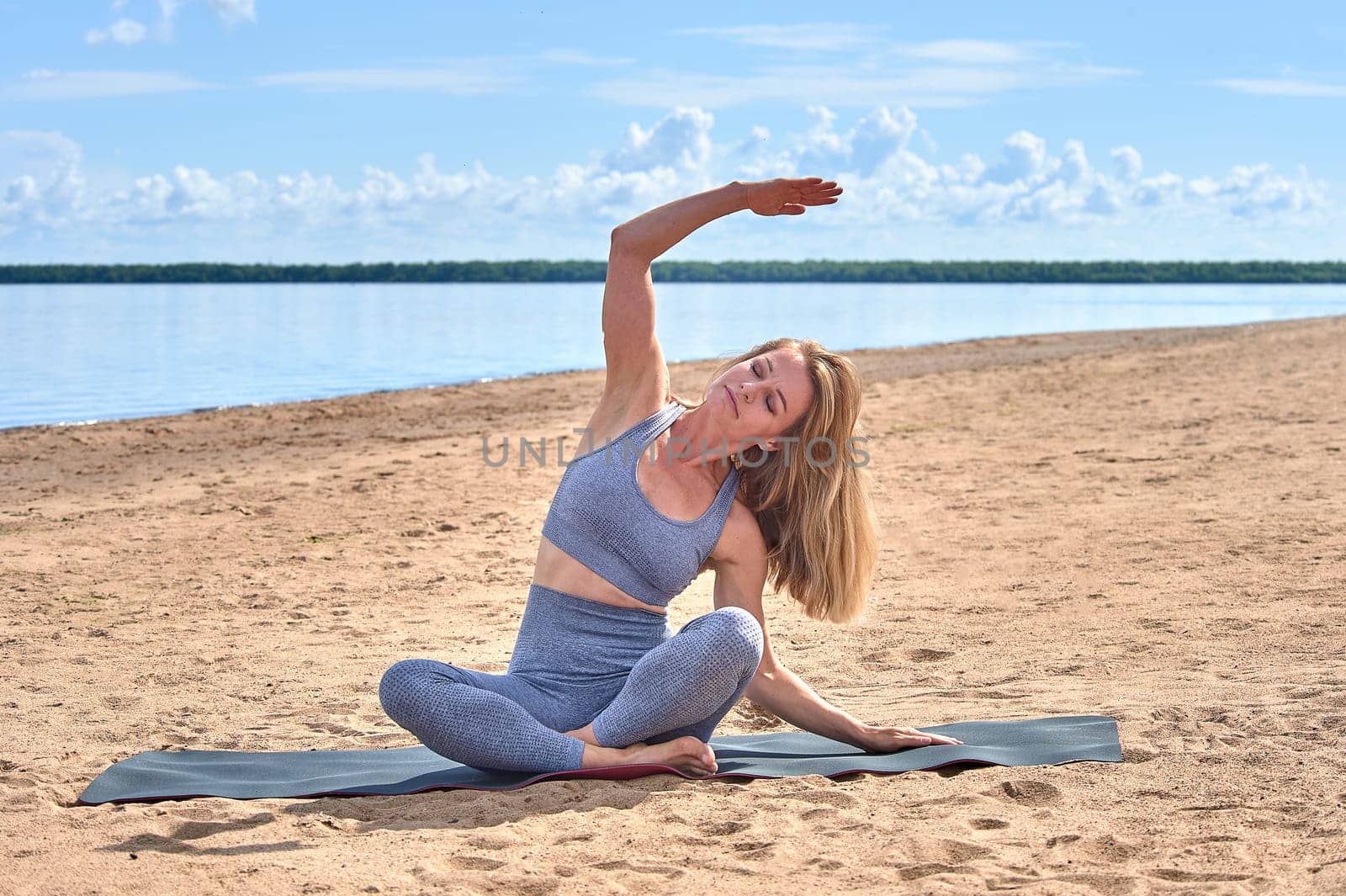 A woman does yoga on a sandy beach against the background of a river. High quality photo