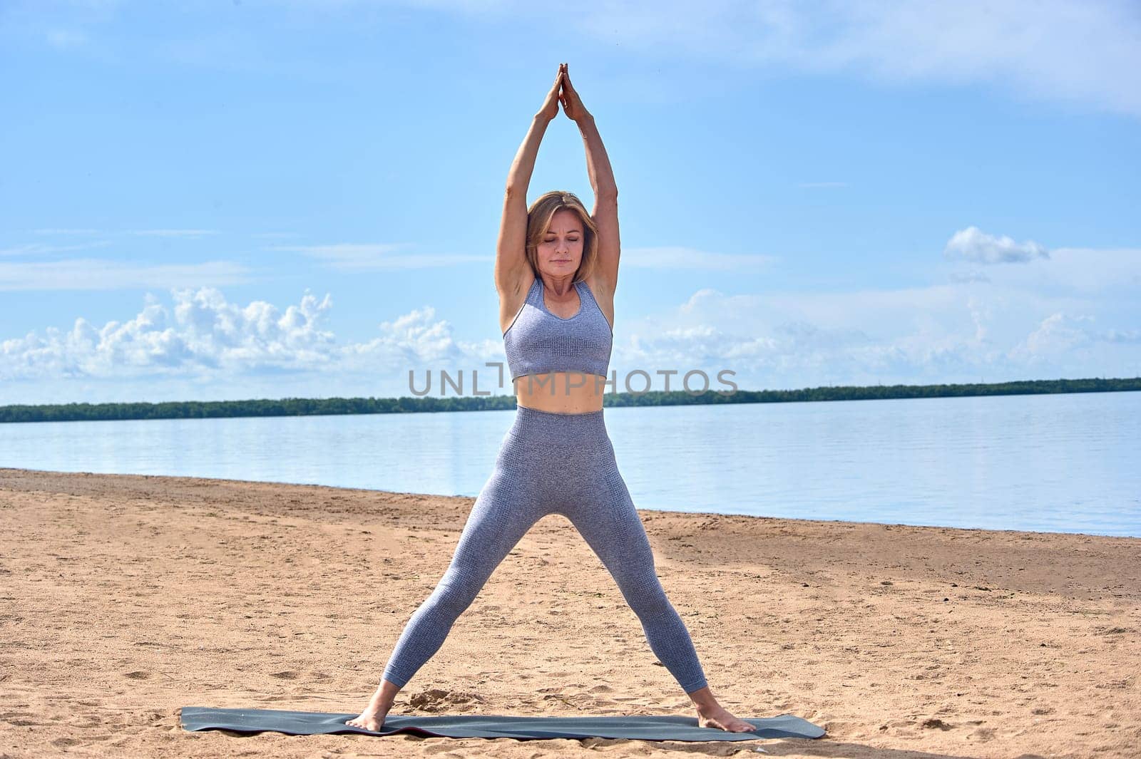 A woman does yoga on a sandy beach against the background of a river. High quality photo