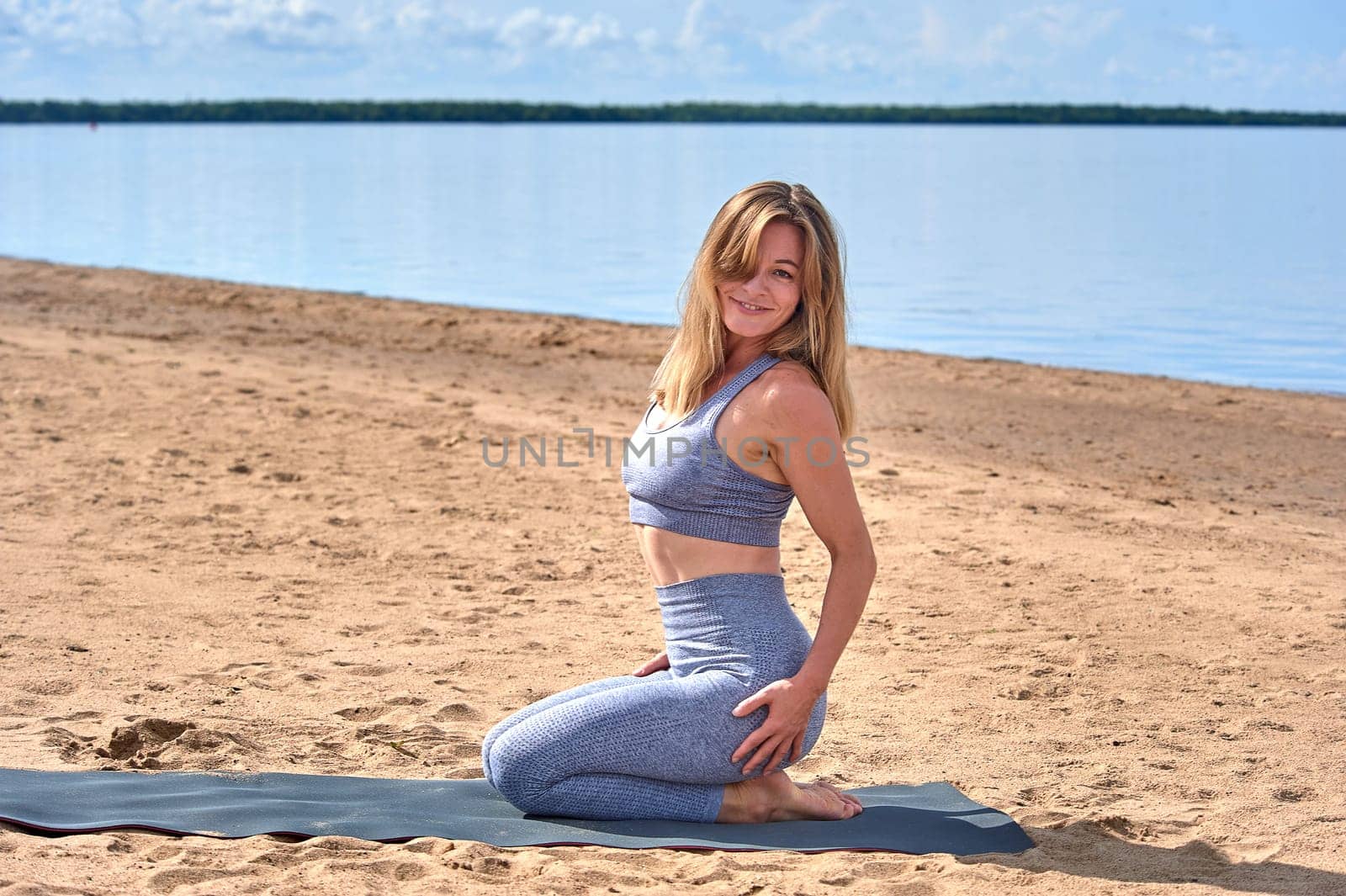 A beautiful woman is sitting on a yoga mat on the beach on a sunny summer day. High quality photo