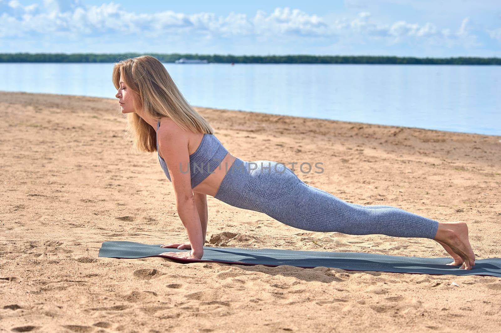 A woman does yoga on a sandy beach against the background of a river. High quality photo