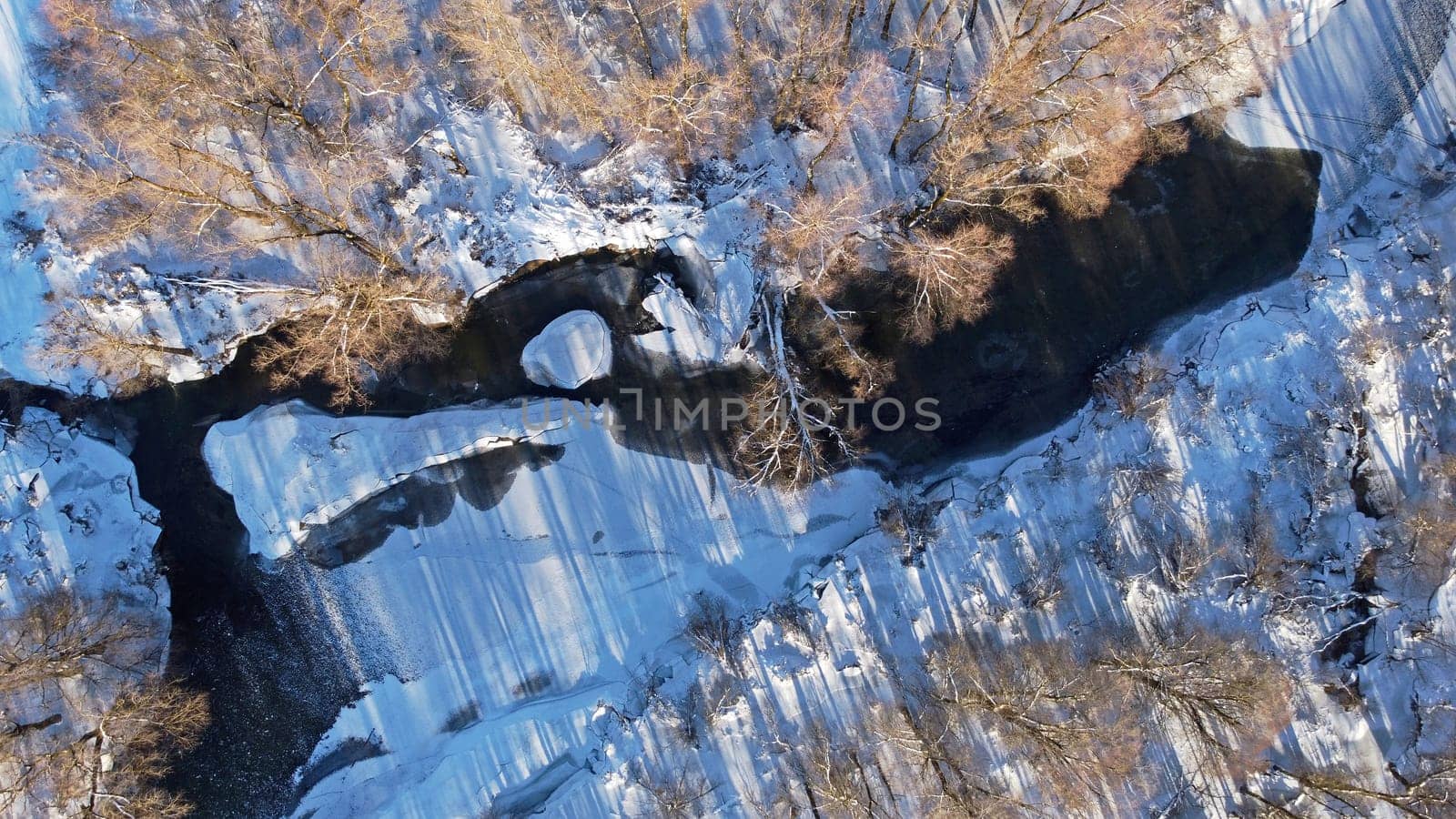 Aerial shot with drone of snowy deciduous forest with stream in winter