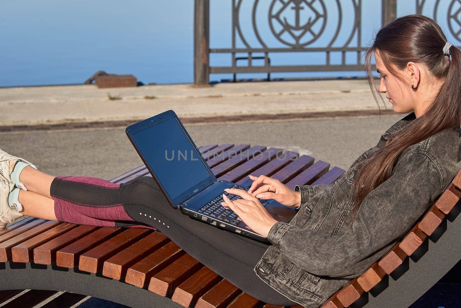 Young woman sitting on a bench with a laptop and working on a sunny summer day. High quality photo