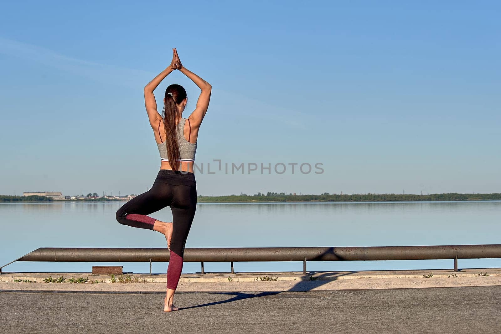 A young woman does yoga on the pier in the early morning, against the background of the river. High quality photo