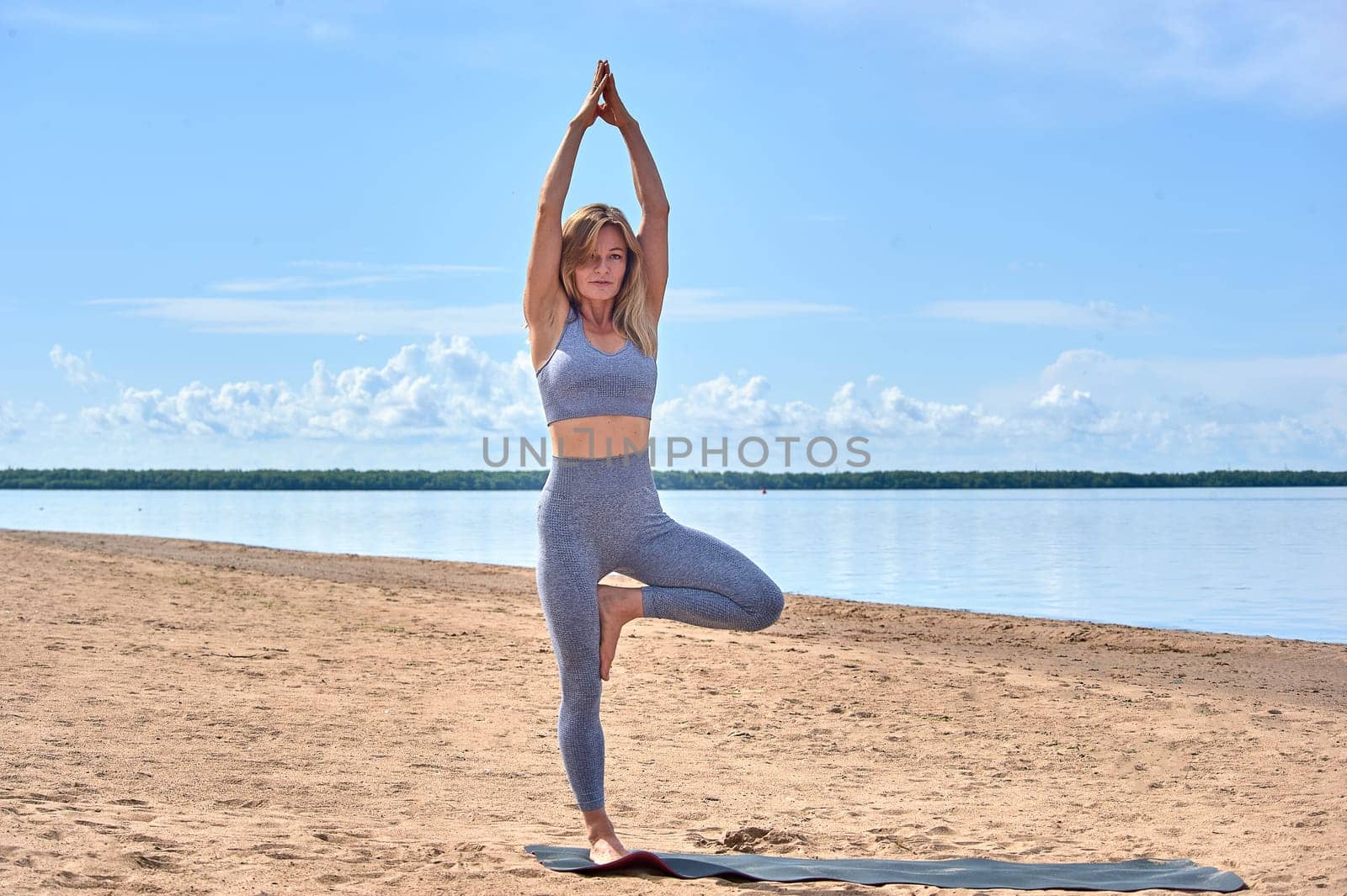 A woman does yoga on a sandy beach against the background of a river. High quality photo