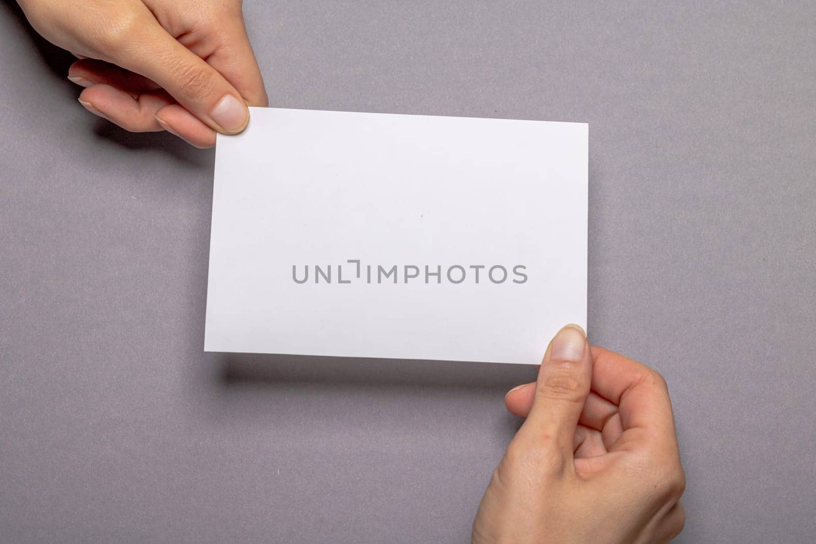 two female hands holding a blank piece of paper with copy space in front of a gray colored background cardboard