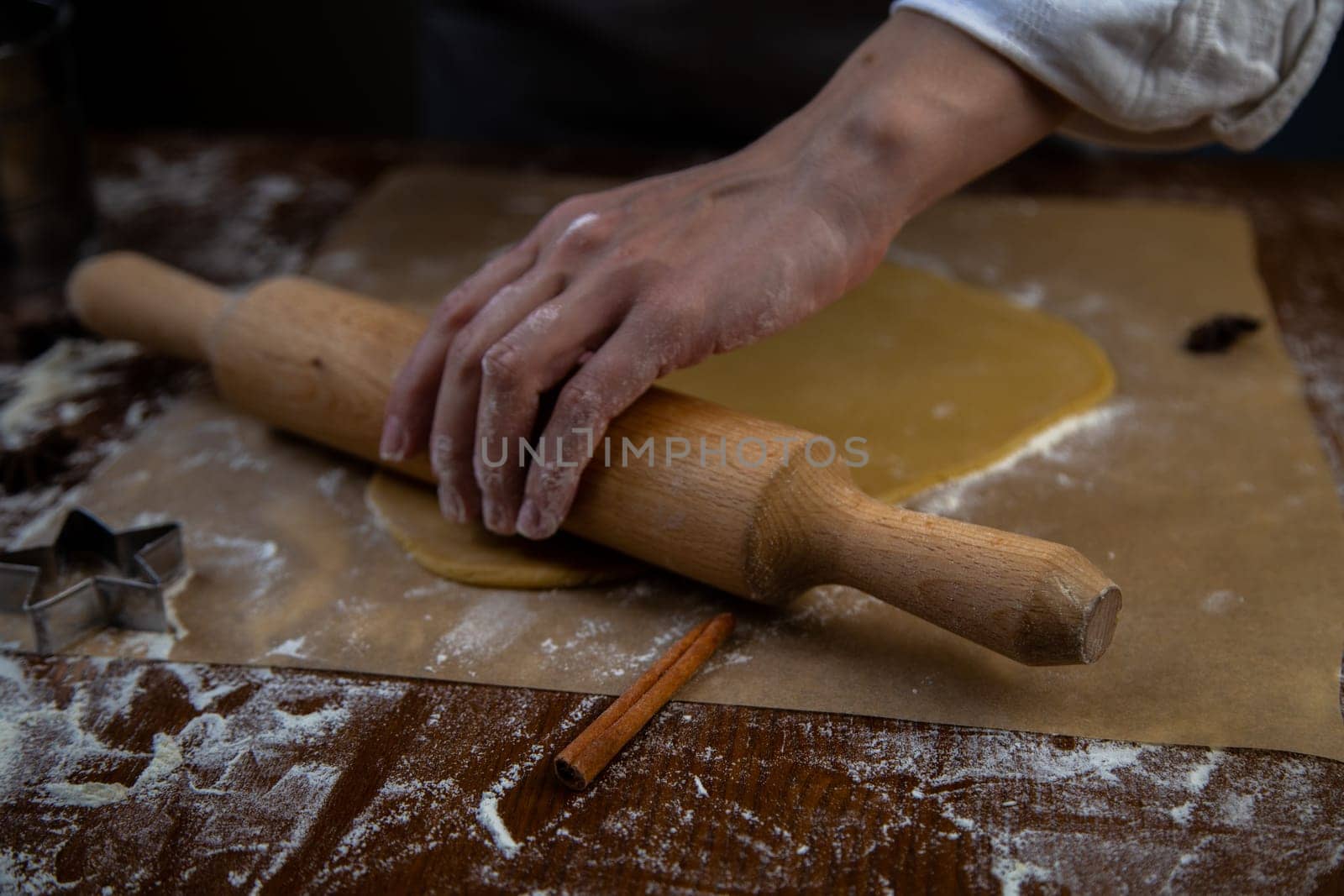 The dough is rolled out with a rolling pin on parchment, flour is scattered around, the photo is in a dark key. High quality photo