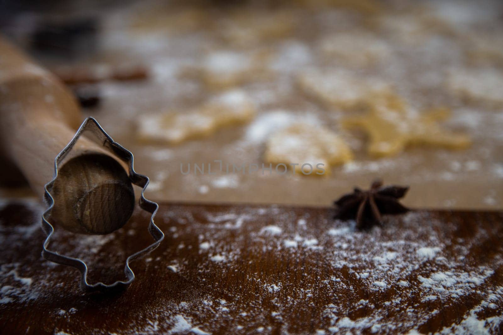 A Christmas tree-shaped mold stands leaning on a rolling pin against a background of cookies, parchment and flour cut out of dough. Photos in dark colors. High quality photo