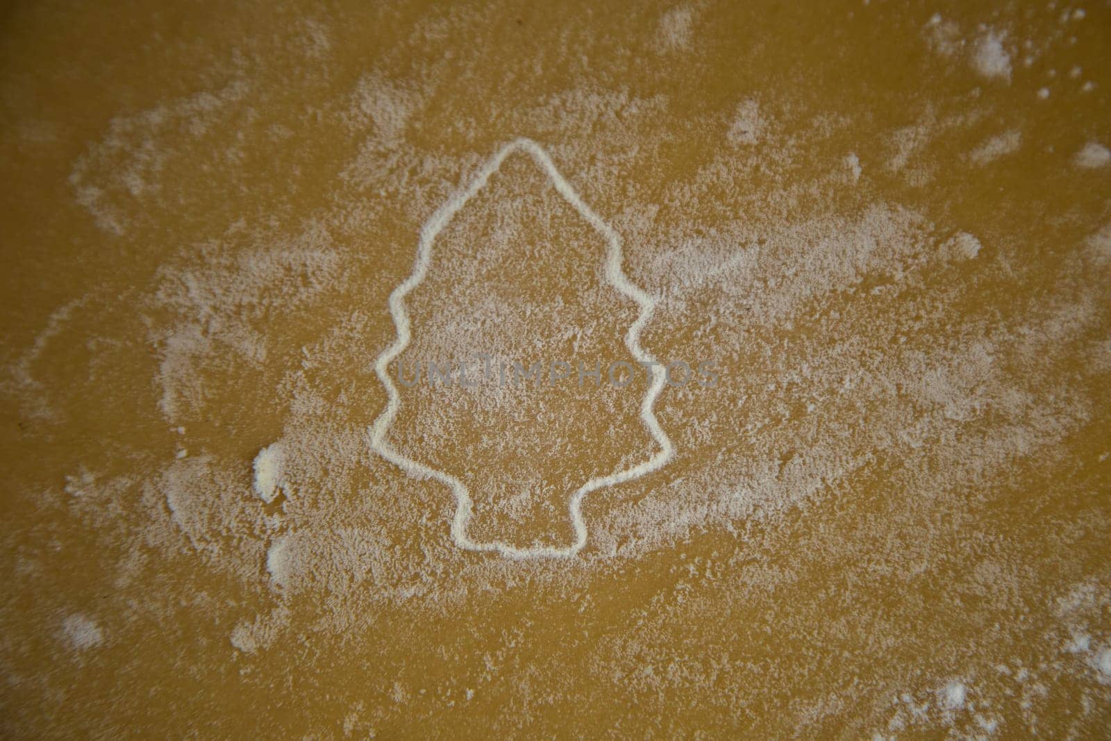 The figure of a Christmas tree is carved on the dough, the contours of which are brightly outlined with flour, the dough is also in flour. High quality photo