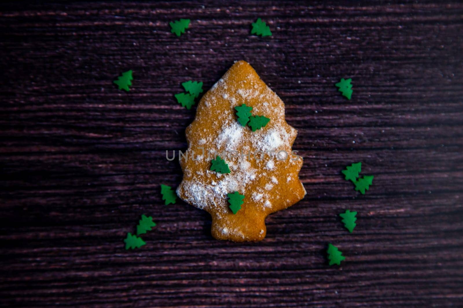 Cookies in the form of a Christmas tree sprinkled on top of white flour and small green Christmas trees on a dark wooden background. High quality photo