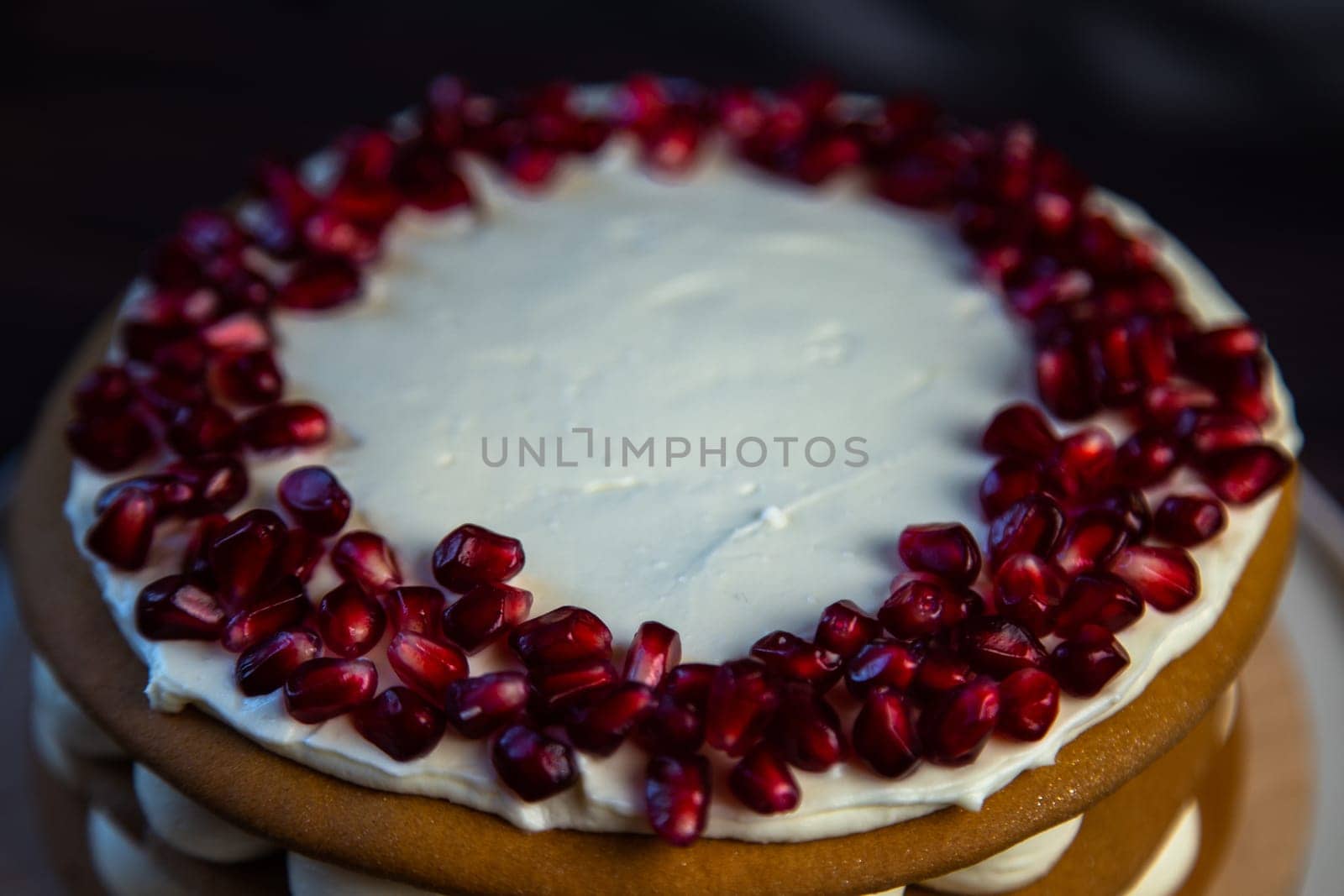 Cake with sponge cakes, decorated with white cream and pomegranate seeds on top in a circle, layers of cream are visible in circles on the side, a close-up view from the side. High quality photo