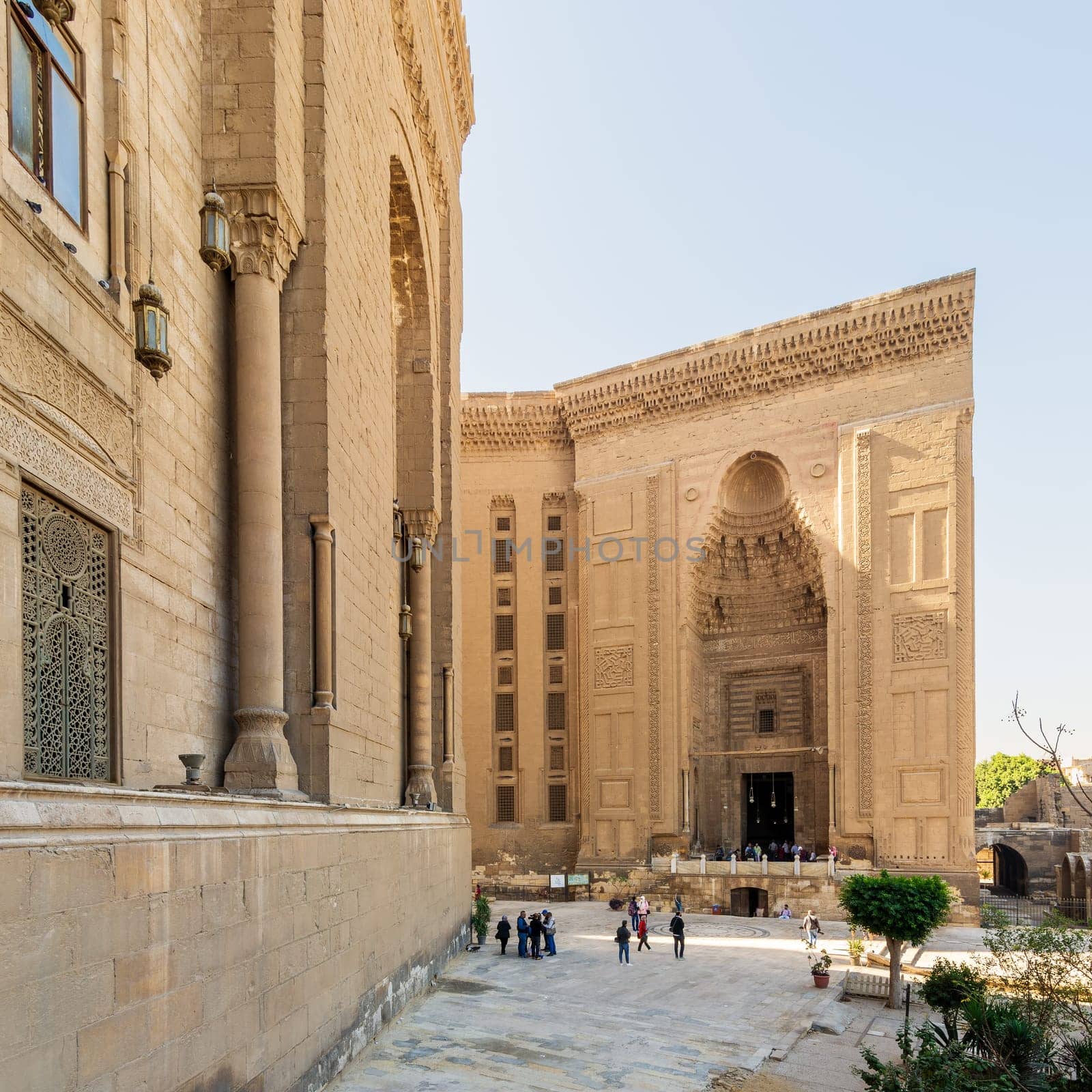 Cairo, Egypt - November 27 2021: Facade of Islamic Mamluk era Mosque and Madrassa of Sultan Hassan, with side facade of royal era Al Rifai Mosque, with few visitors, Old Cairo