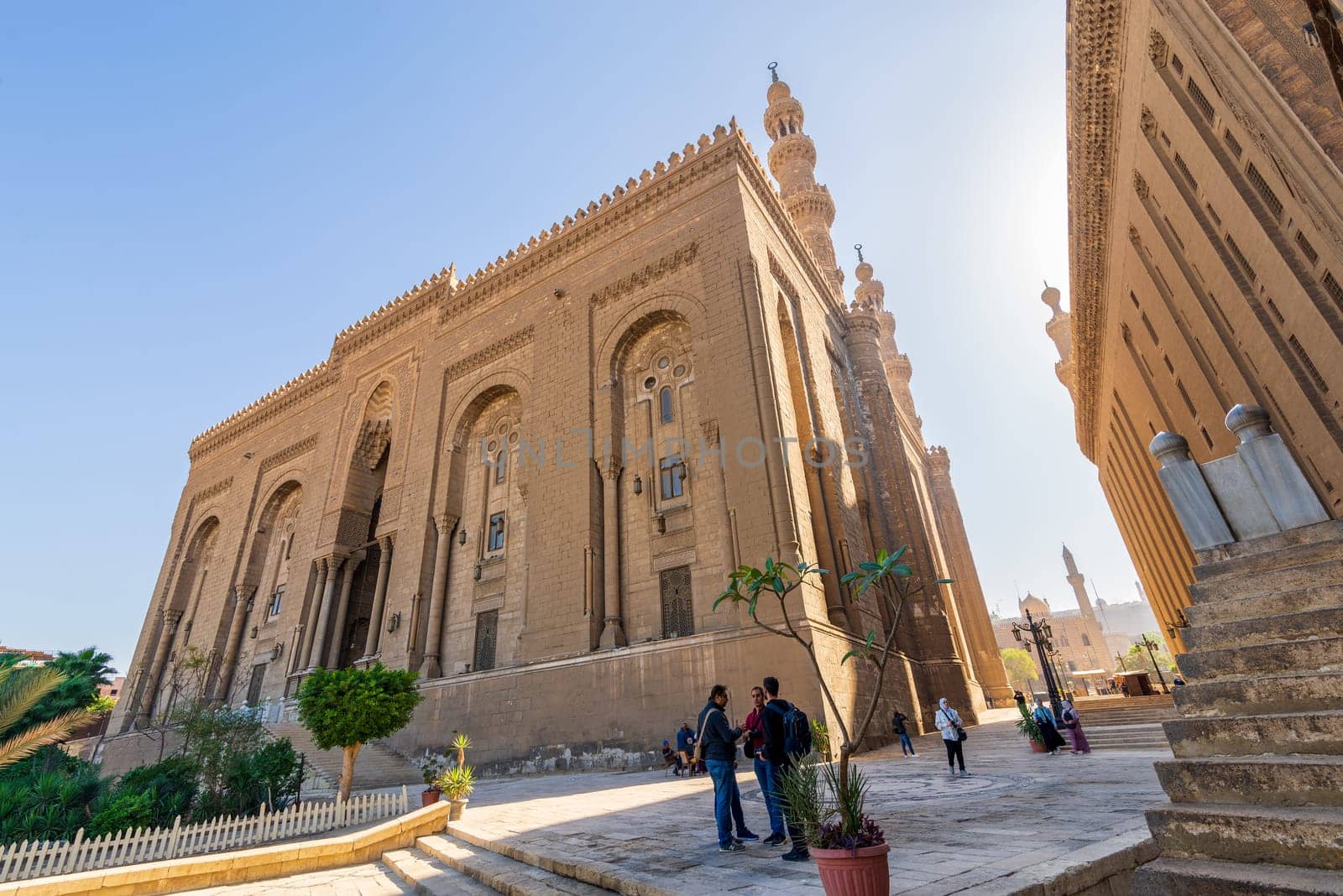 Cairo, Egypt - November 27 2021: Facade of Islamic Royal era Mosque of Al Rifai, with side view of Mamluk era Mosque and Madrassa of Sultan Hassan, with few visitors, Old Cairo