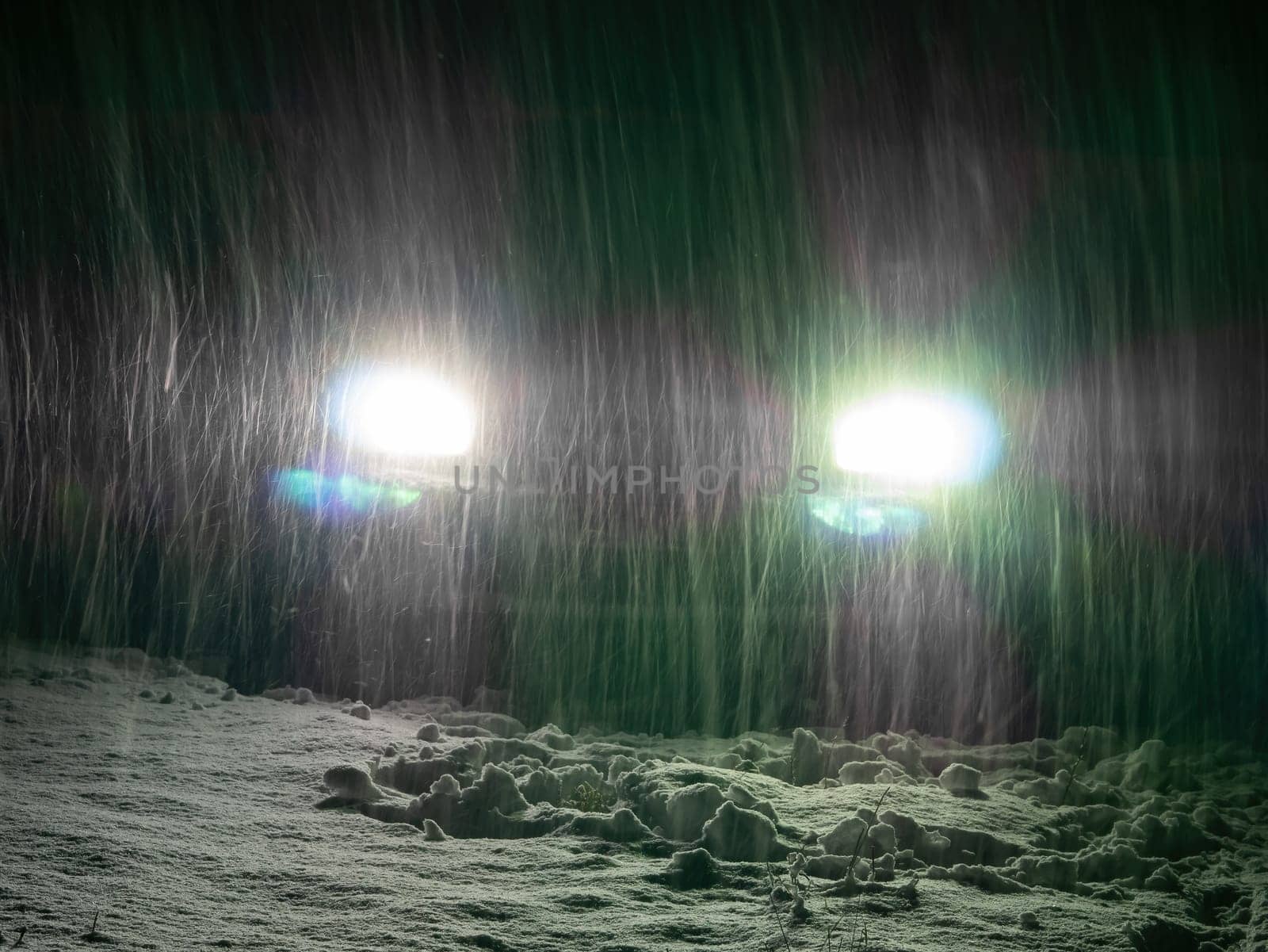 Snow blizzard in the light of car headlights on the night road. Falling white snow. Car headlights. Night automobile road. Winter season. Ice on the track. Frosty weather. Driving in winter.