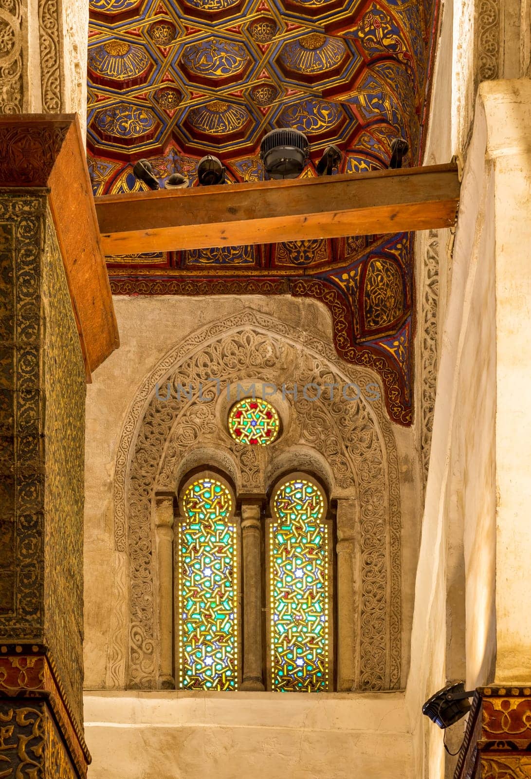 Two adjacent perforated stucco arched windows decorated with colorful stain glass with geometrical and floral patterns, at Mamluk era public historical Qalawun complex, Moez Street, Cairo, Egypt