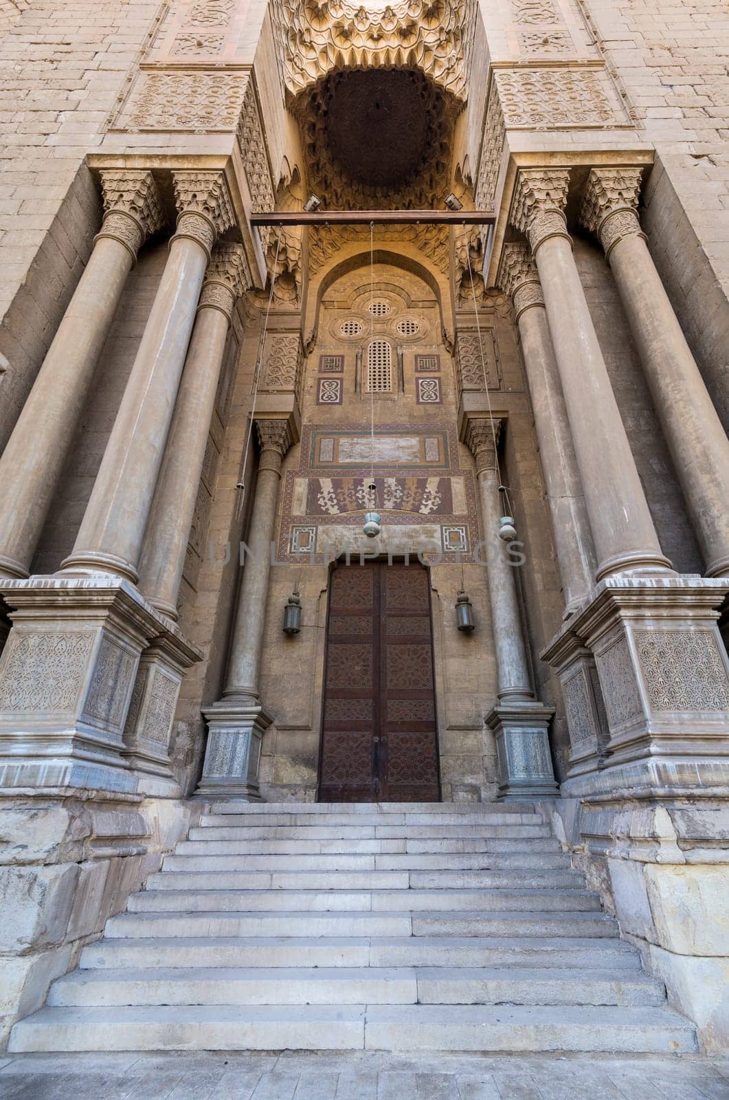 Side gate at al Rifai Mosque, old decorated bricks stone wall with arabesque decorated wooden door framed by marble engraved cylindrical columns, Medieval Cairo Egypt