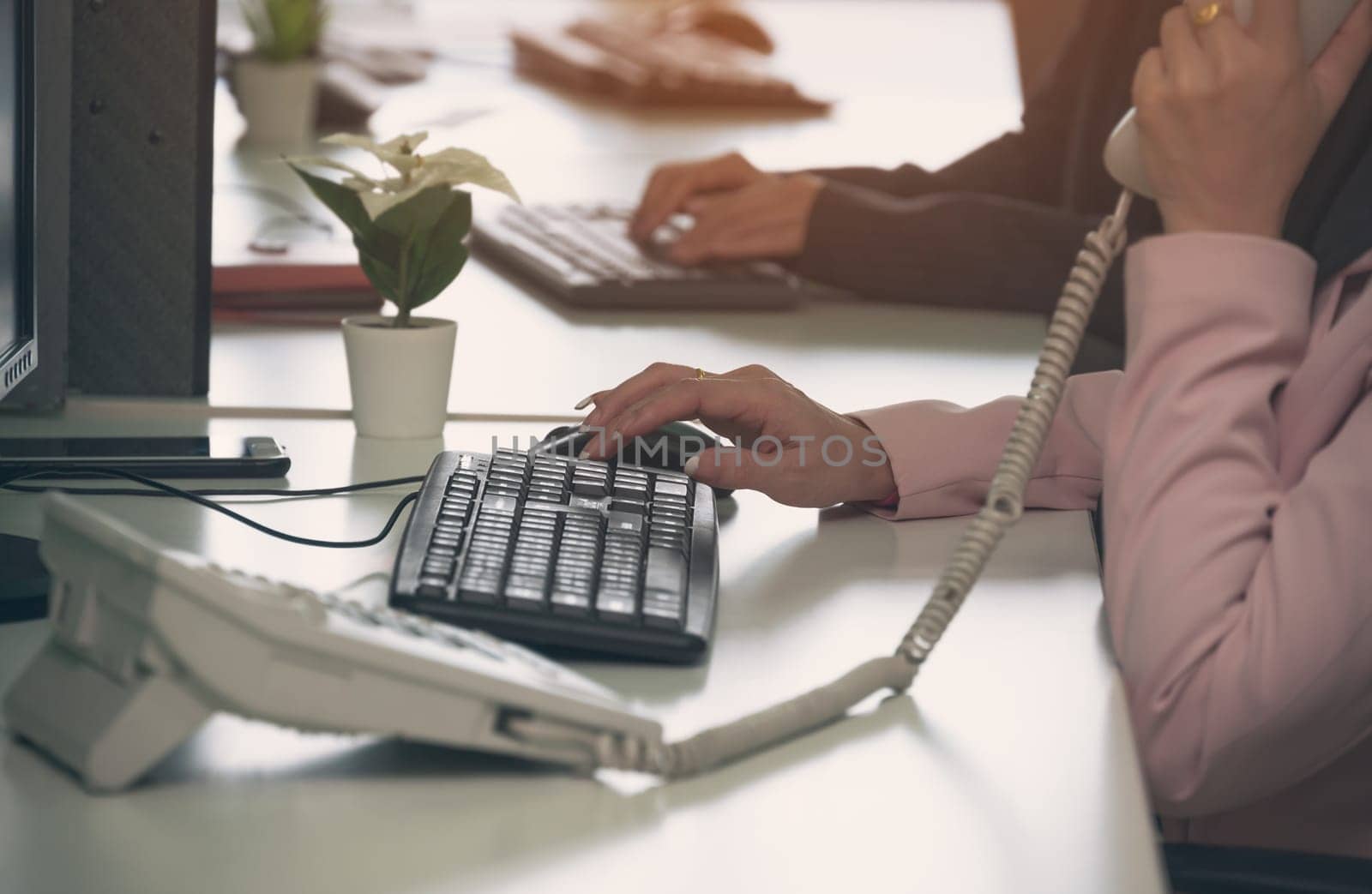 Woman talking on telephone while working on computer at desk. Busy work at office workplace concept