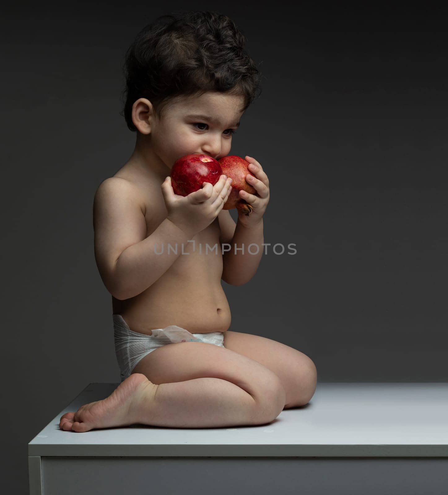 One year old boy with diaper holding two pomegranate in front of mouth