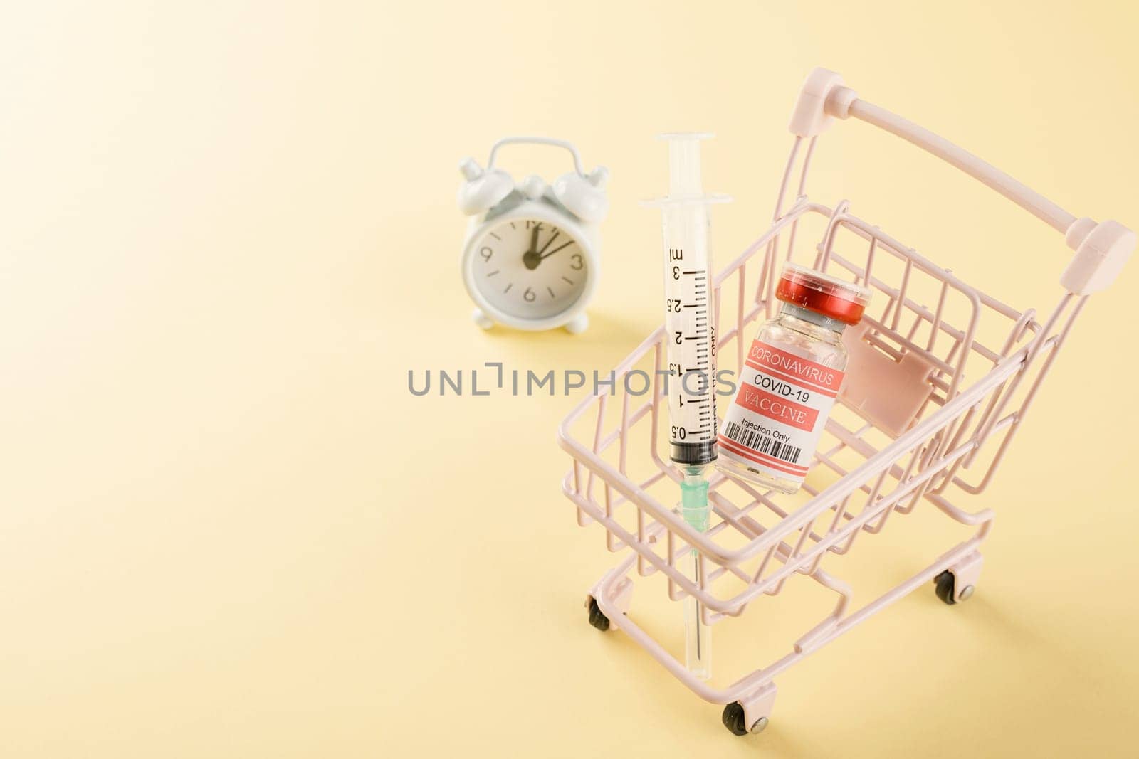 Shopping cart with vaccine vials bottles and syringes for vaccination against coronavirus, medicine illness, COVID-19 disease vaccine studio shot isolated on yellow background