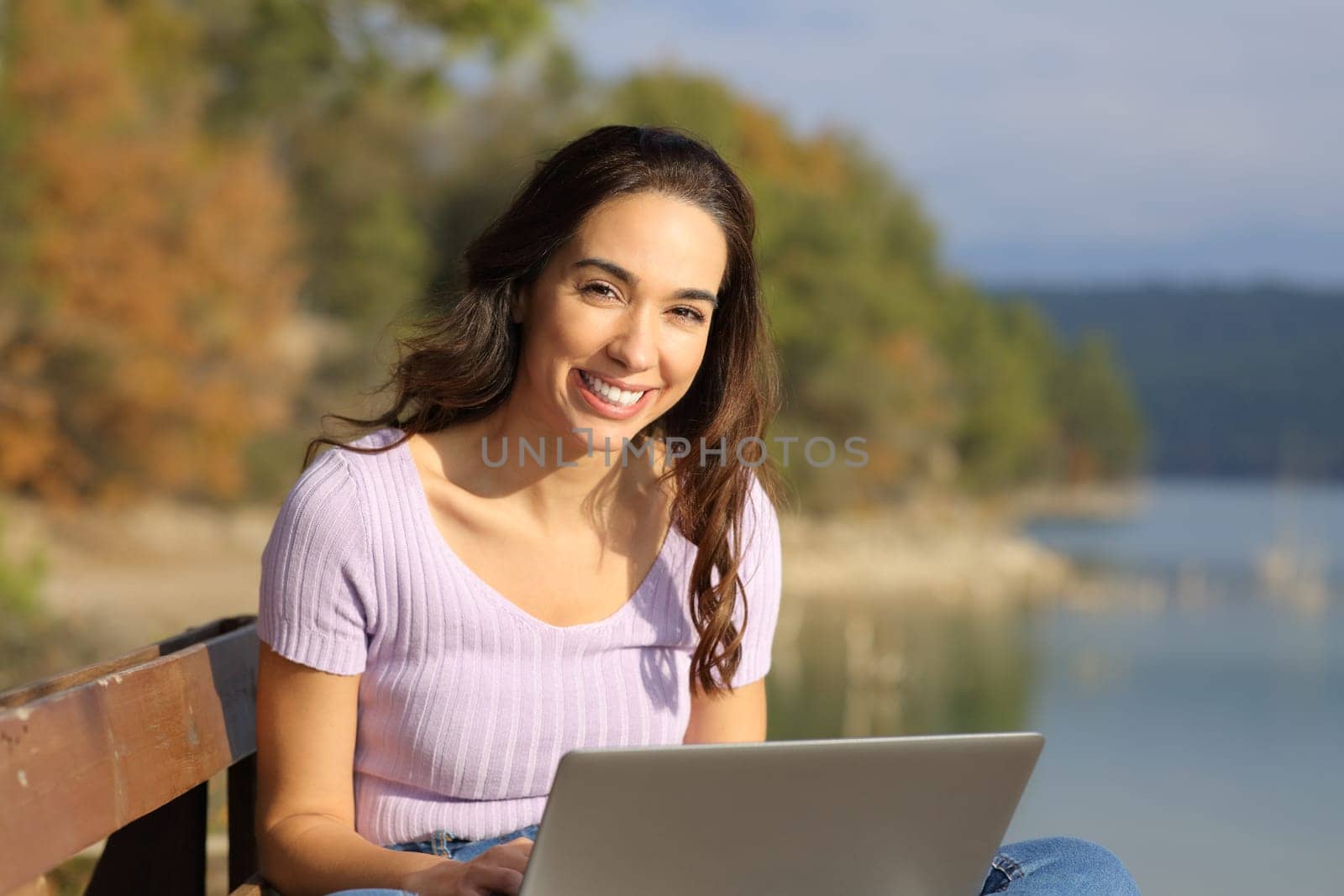 Happy woman with a laptop looks at you sitting outdoors in the mountain