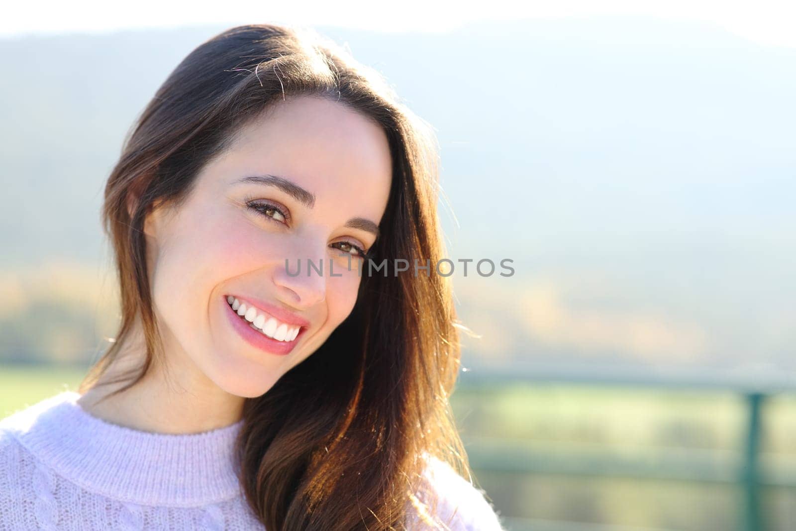 Happy woman with perfect smile looks at camera outside a sunny day