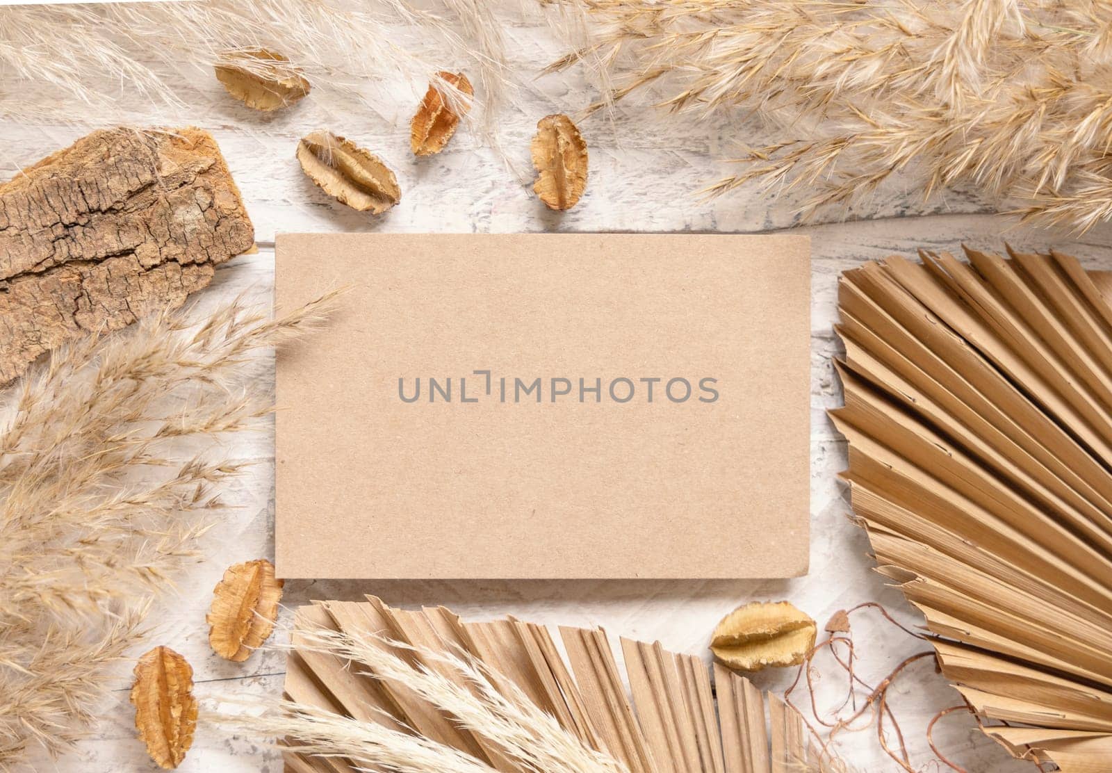 Blank card on white wooden table near dried plants, palm leaves and pampas grass top view. Boho scene with horizontal paper card flat lay. Greeting or Invitation card mockup, place for text