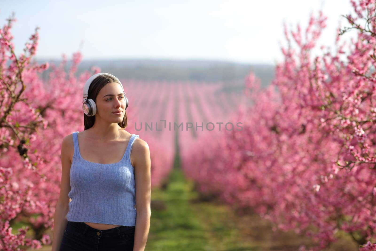 Front view portrait of a beautiful single woman walking in a field listening to music wearing headphones