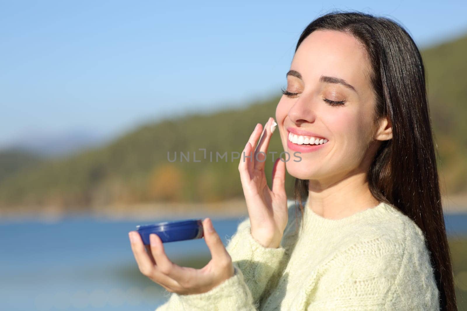 Happy woman in winter moisturizing her cheek in the mountain