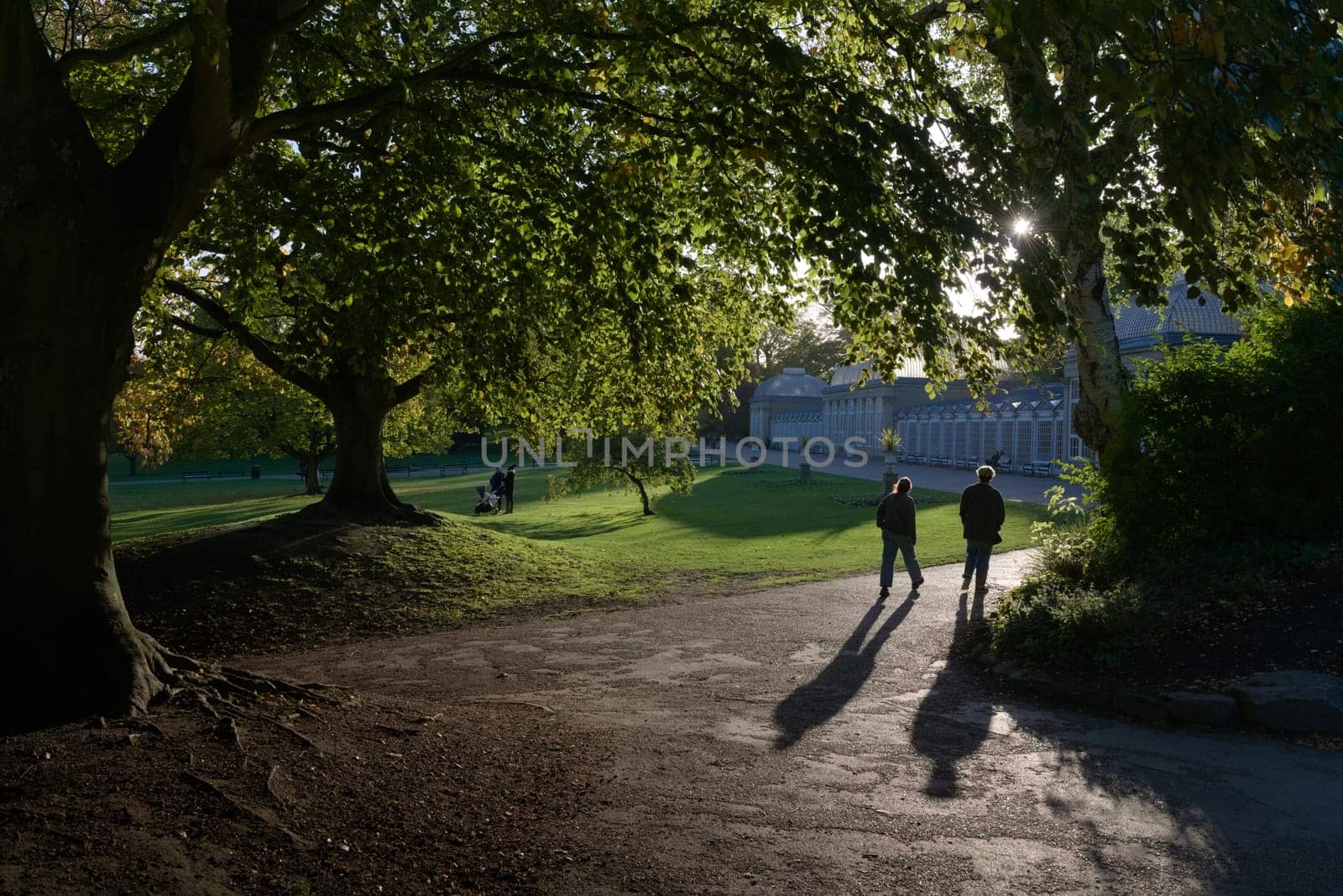 Sheffield, United Kingdom, 21st October, 2021: A silhouetted couple walk towards iconic greenhouses near main entrance of sheffield botanical gardens