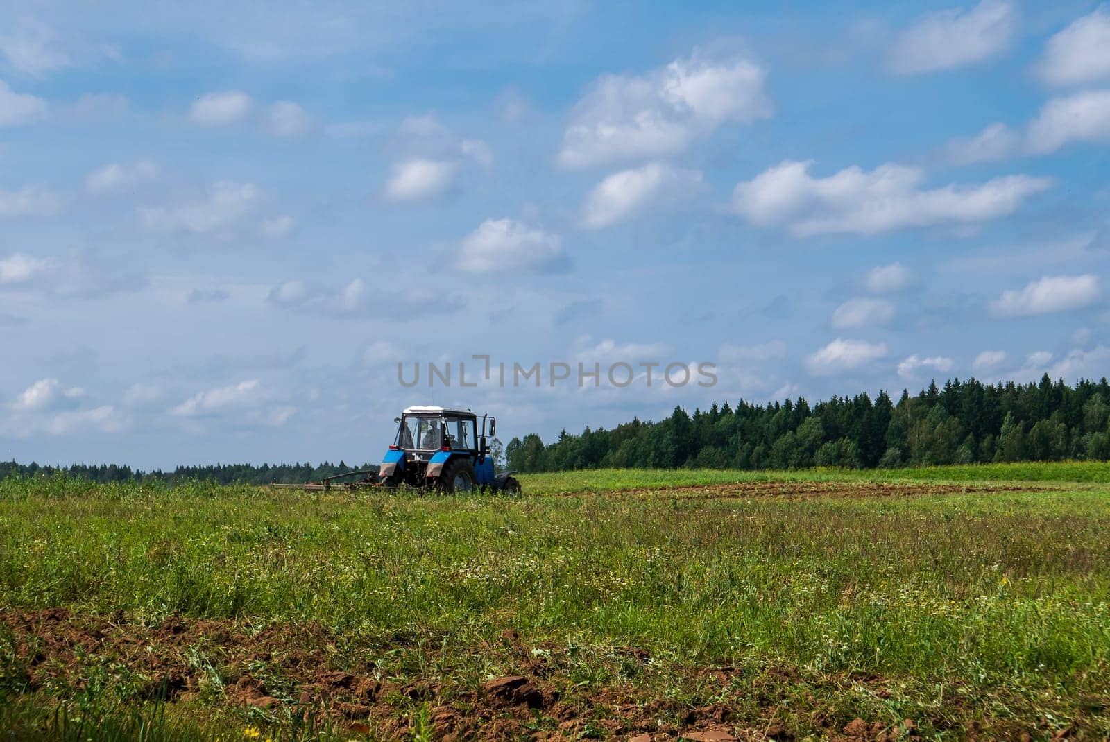 Tractor working in the field, plowing the land, preparing for sowing. View of the field and tractor in the distance against a blue sky with clouds